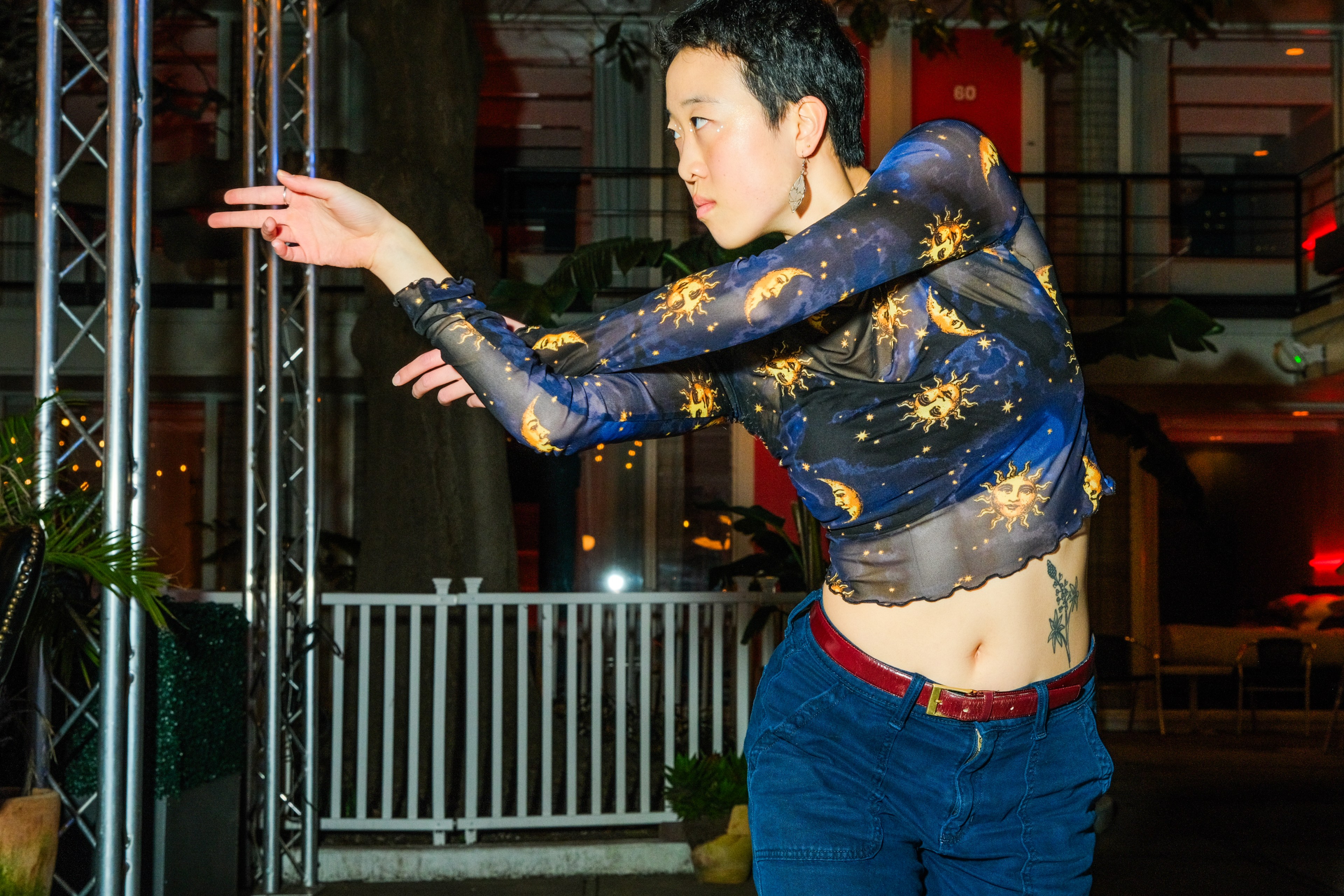 A person in a celestial-patterned top poses with an extended arm, appearing focused and expressive.