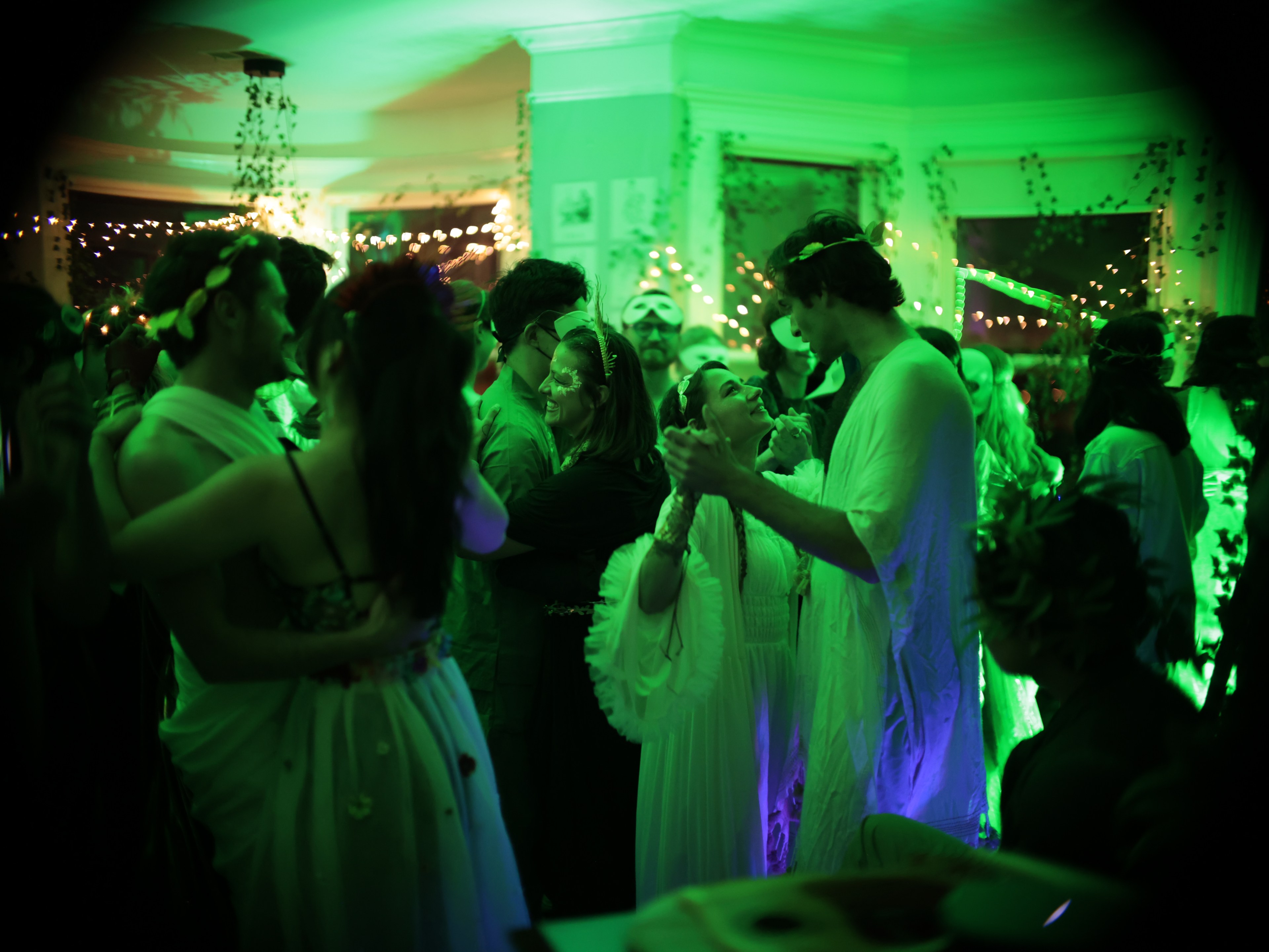 Couples dance in a room with green lighting, decorations and string lights.
