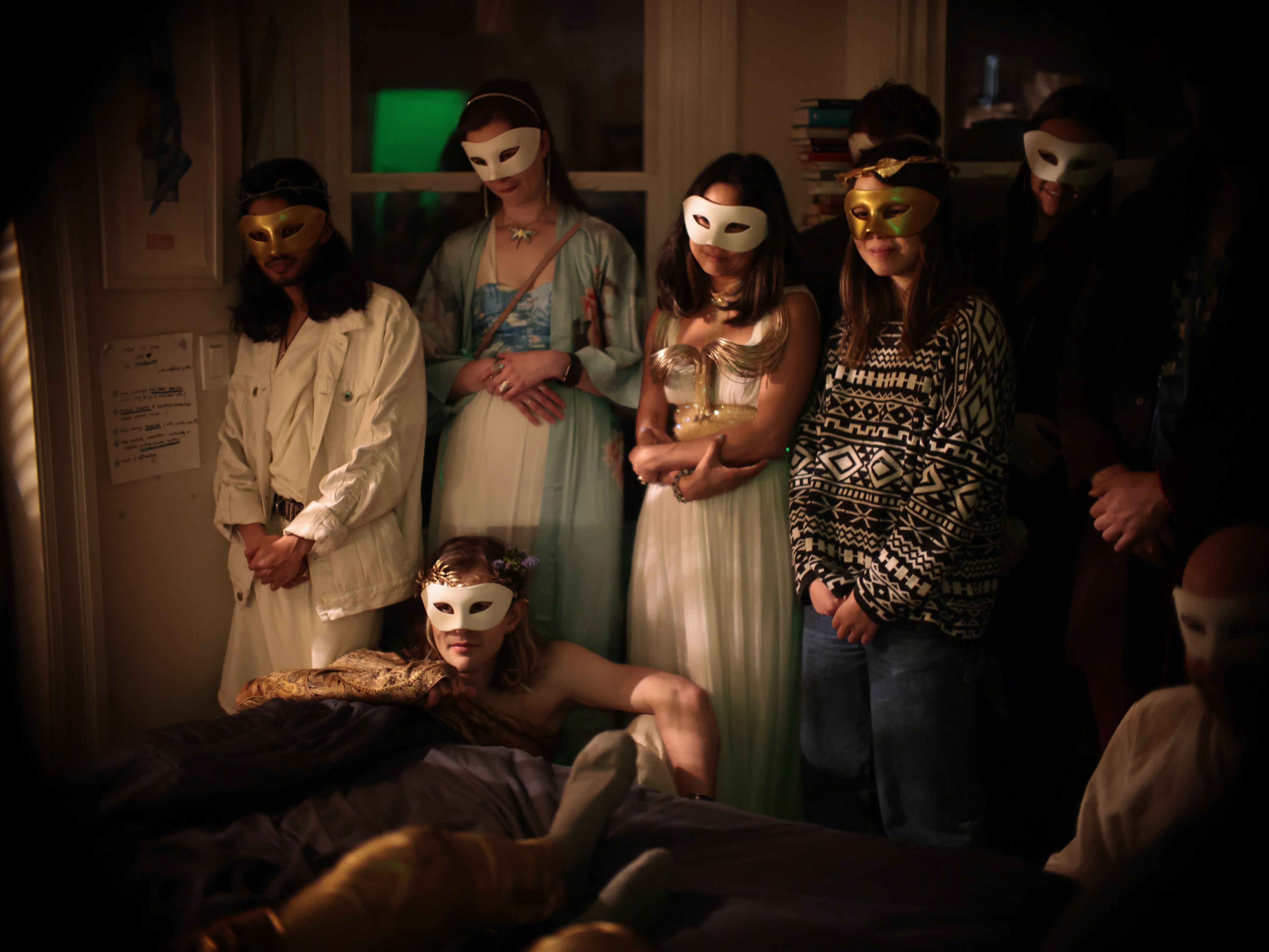 Group of people in masks in a dimly lit room, some standing, one lying down.