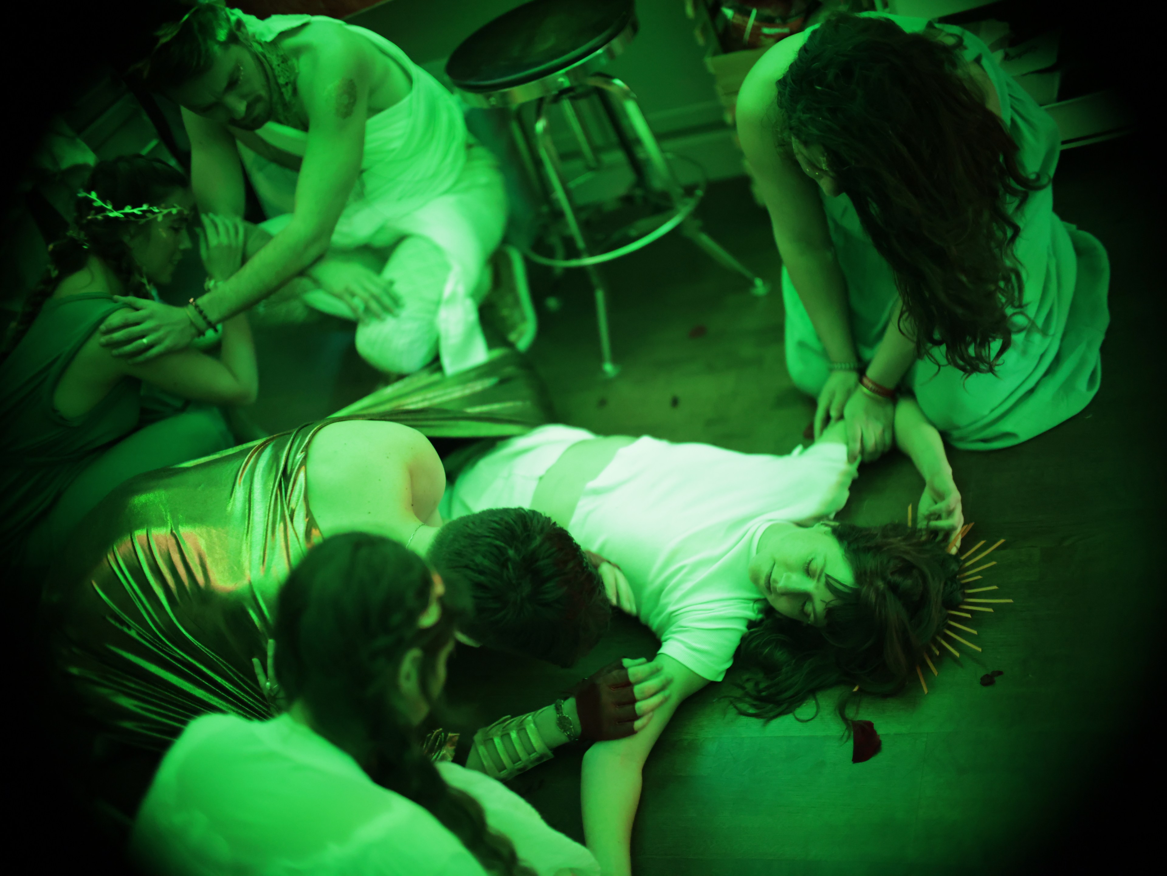 People in a green-lit room seem distraught, one lying on the floor as others attend to them.
