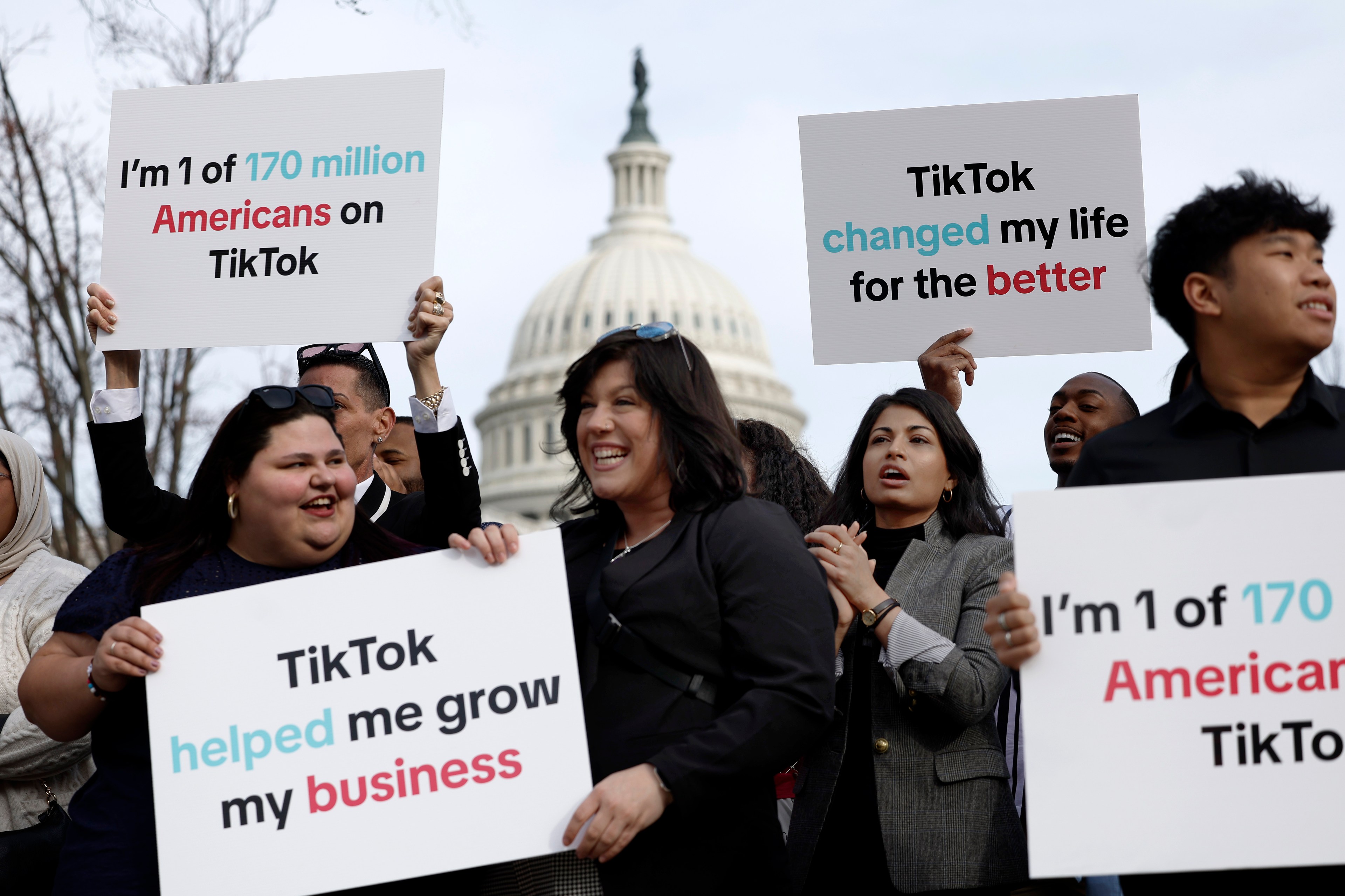 People hold signs praising TikTok outside the domed U.S. Capitol building.