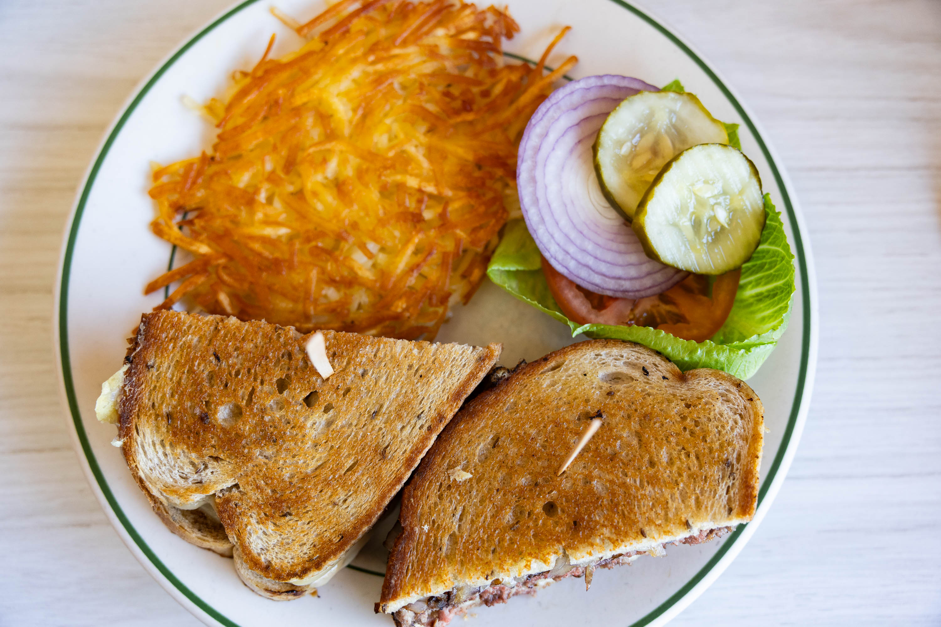 A patty melt sandwich cut in half with hash browns and a fresh side salad on a white plate.