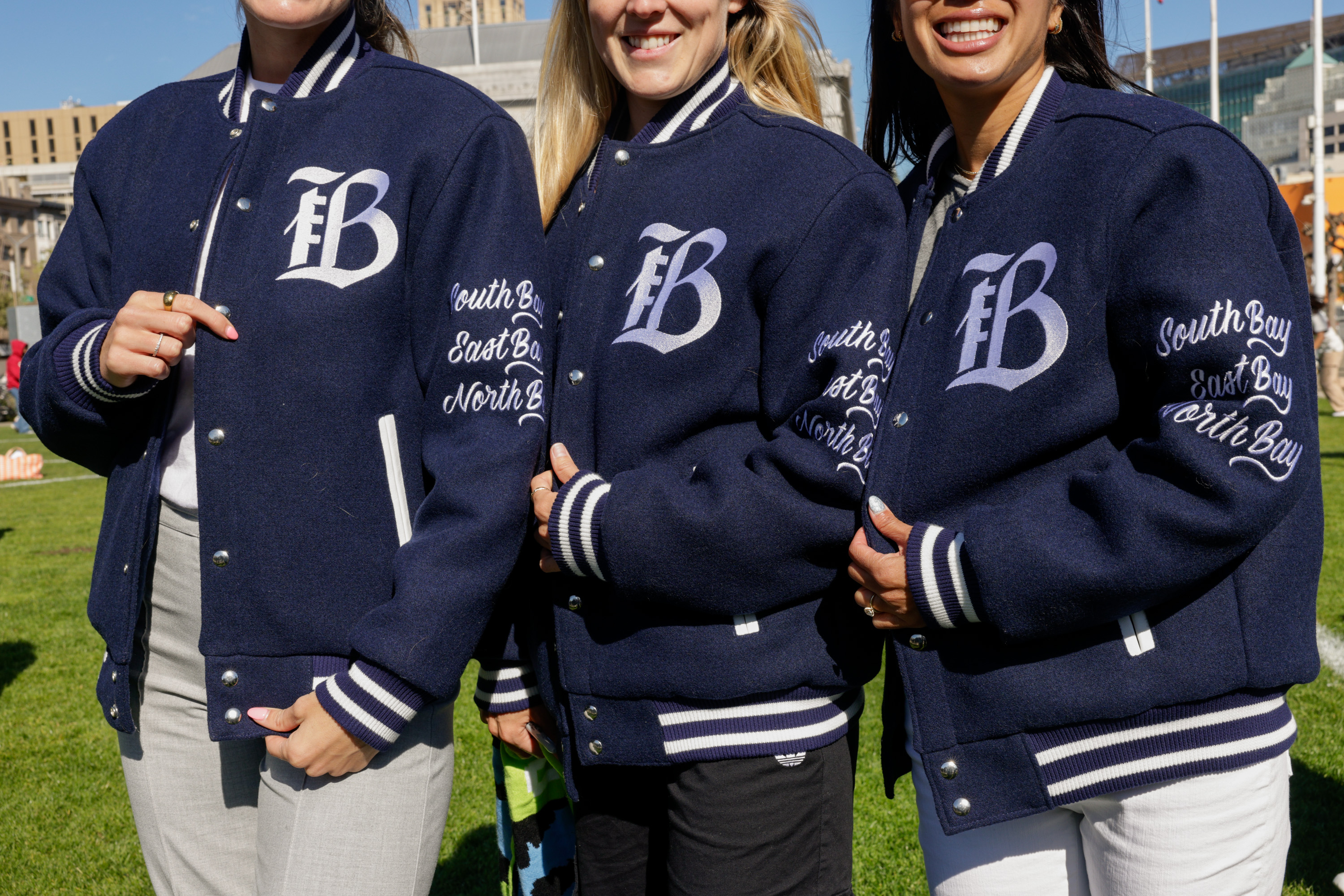 Three people in varsity jackets with &quot;fB&quot; logos, smiling without showing faces, outdoors.