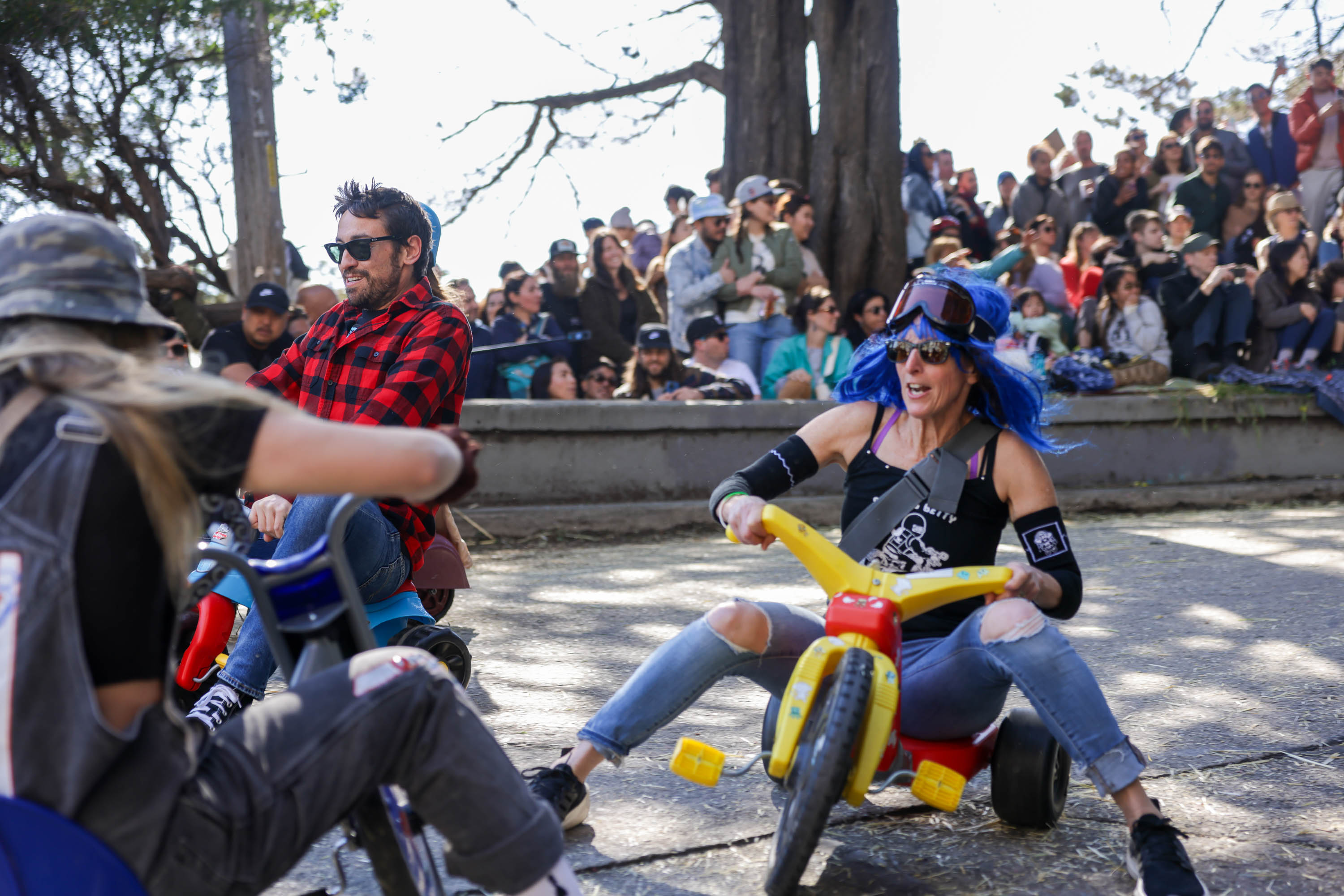 Adults race on children's tricycles before a crowd, displaying fun and competition.