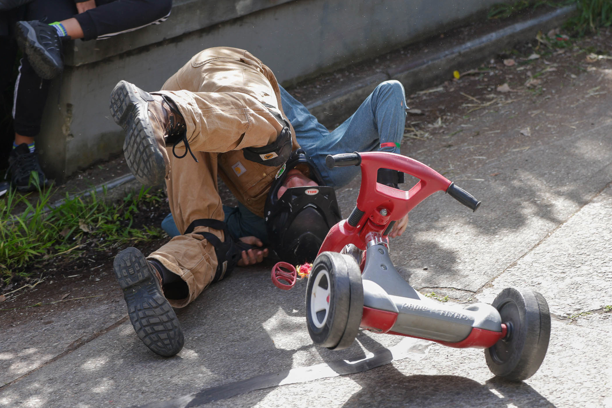 A person is on the ground next to an overturned tricycle, appearing to have fallen.