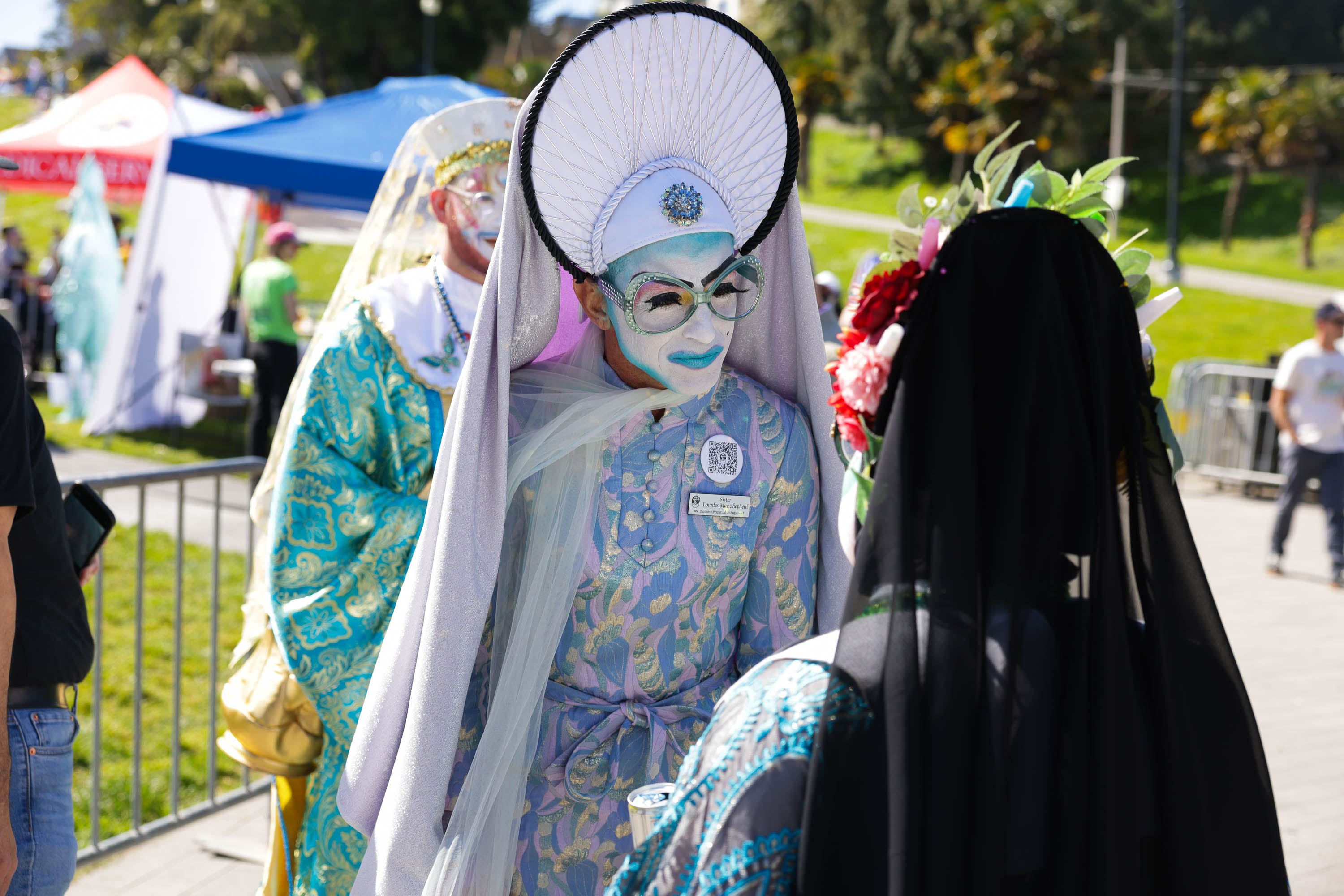 Individuals in elaborate costumes with face paint, one with a headdress, at an outdoor event.