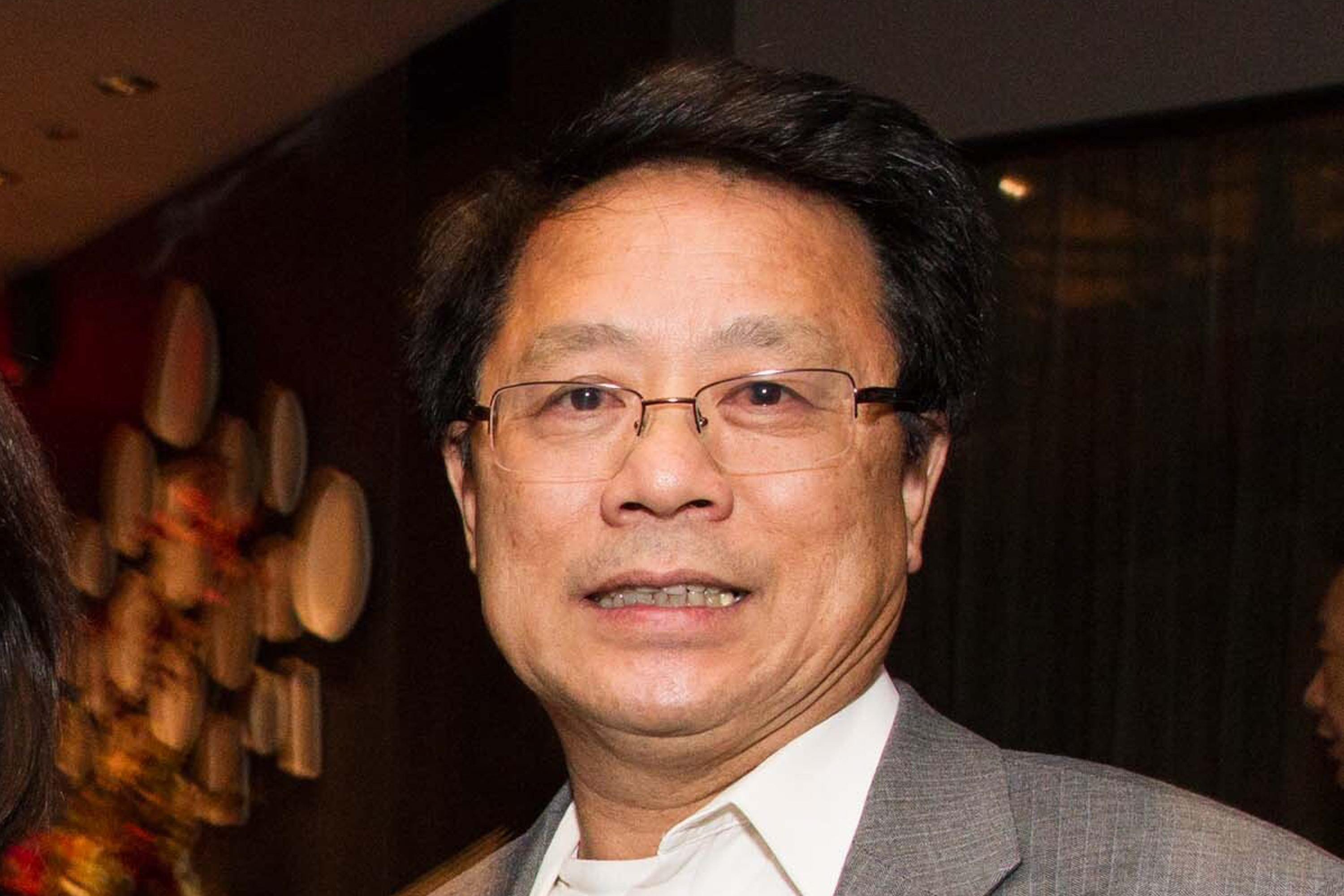 A smiling middle-aged man with glasses, wearing a suit.