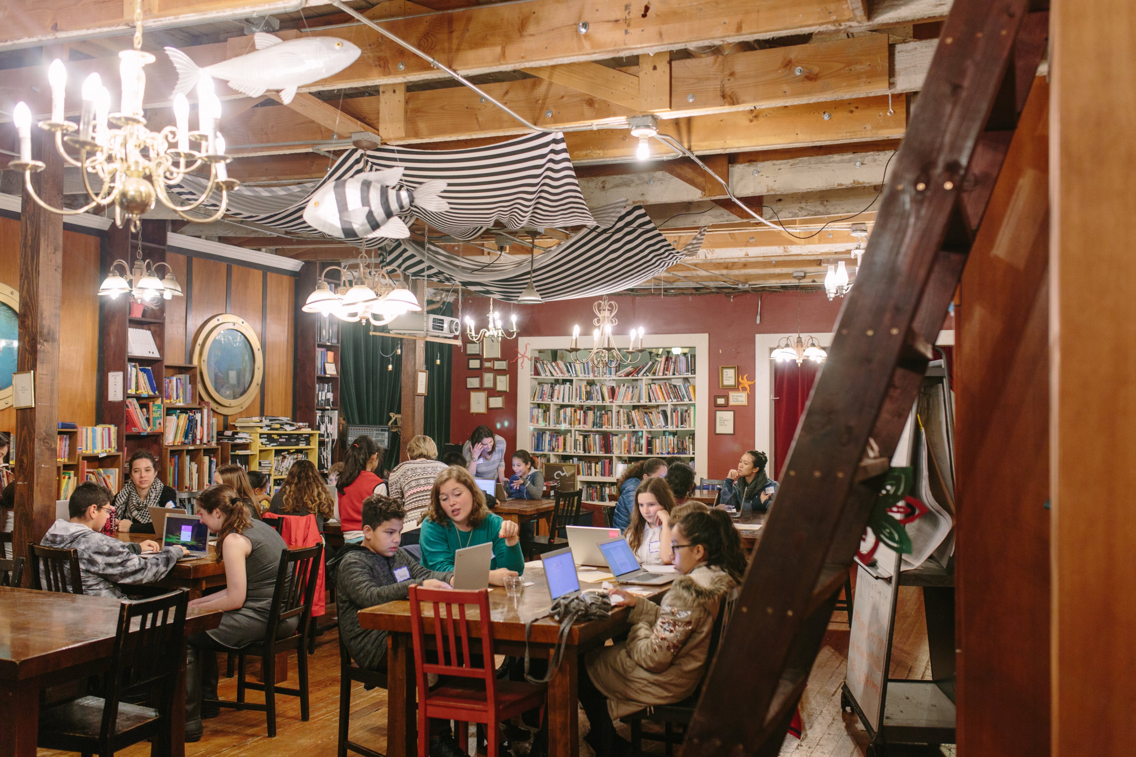 Young people sit at a long table with papers in front of them with chandeliers and artifacts hanging from the ceiling.