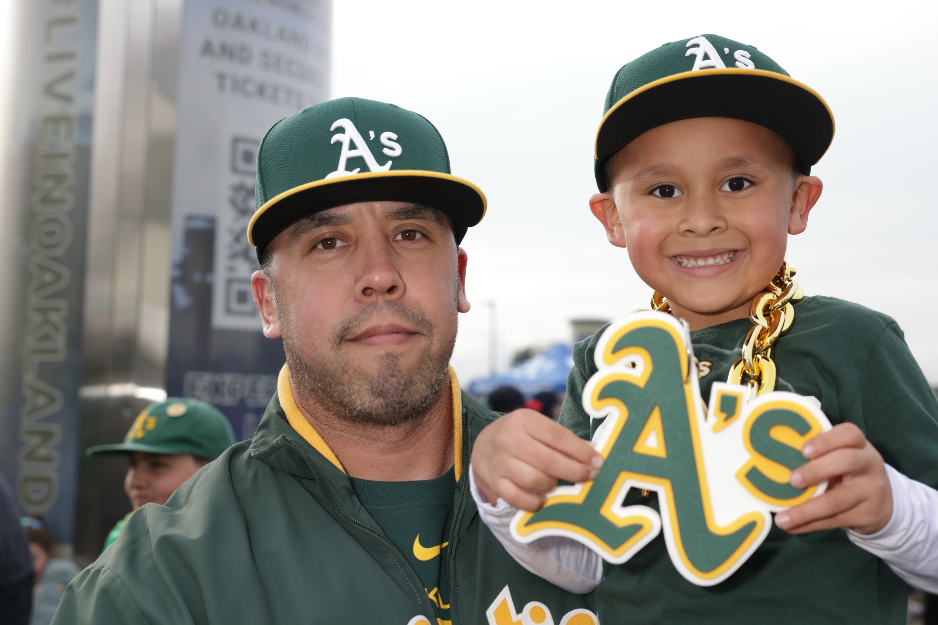 A man and a smiling boy in Oakland A's gear with foam fingers.