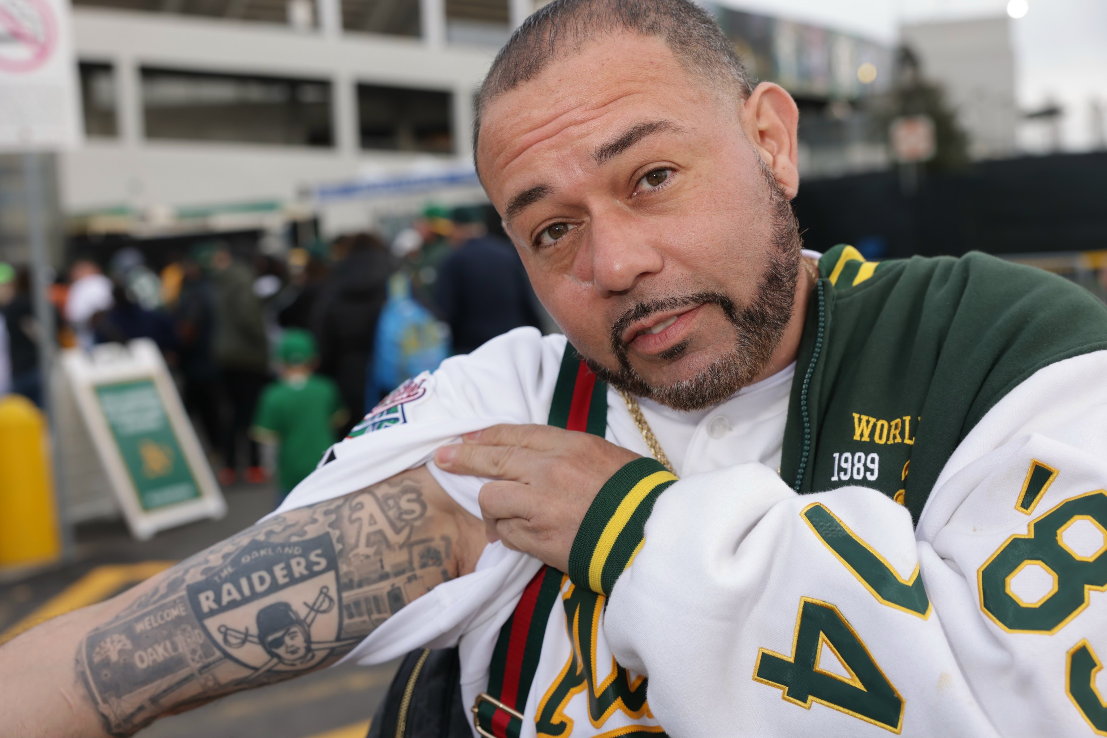 A man in sports attire displays a tattooed arm with &quot;Raiders&quot; and Oakland landmarks.