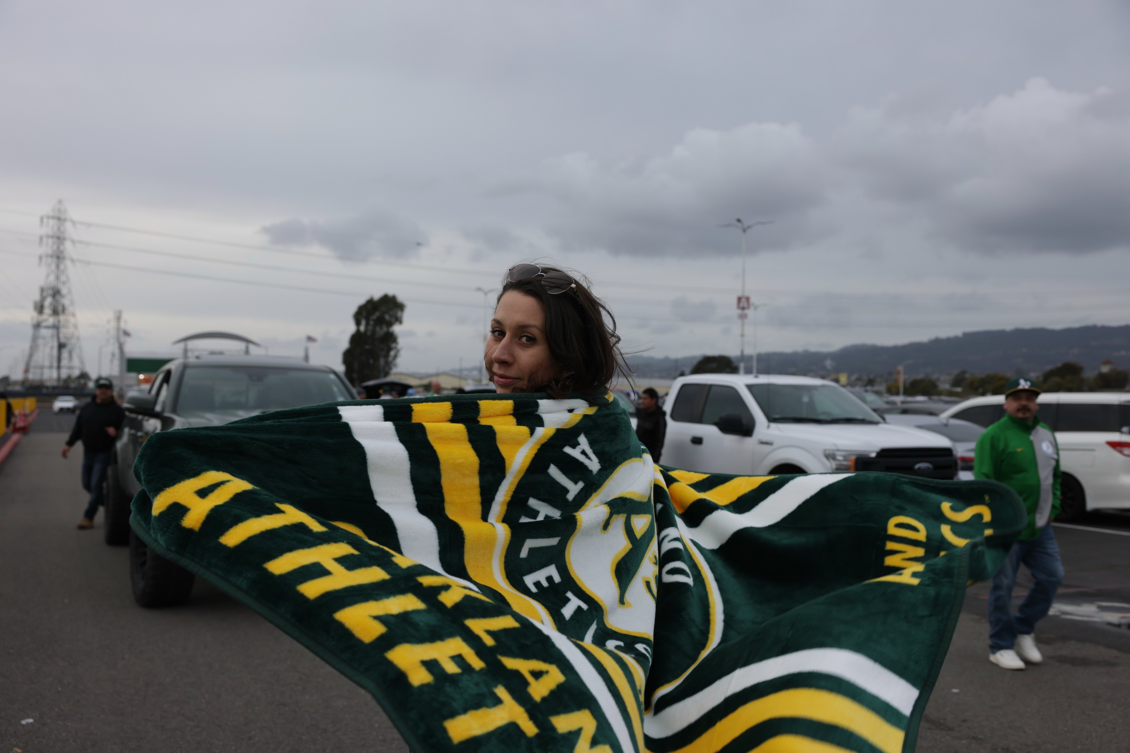 A person holds a green and yellow scarf with the word &quot;ATHLETICS&quot; while standing in a parking lot.