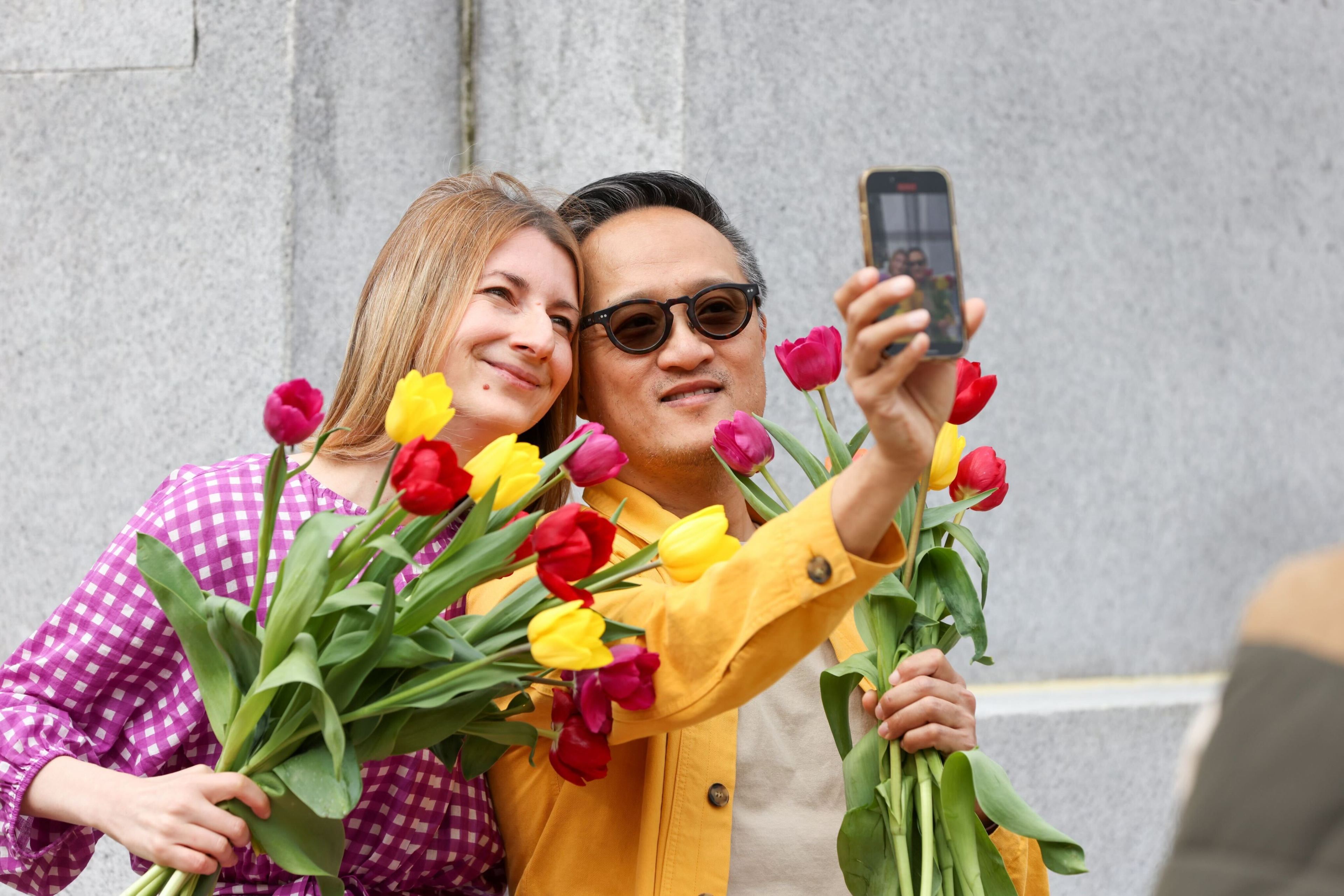 A man and woman taking a selfie with a bouquet of colorful tulips.