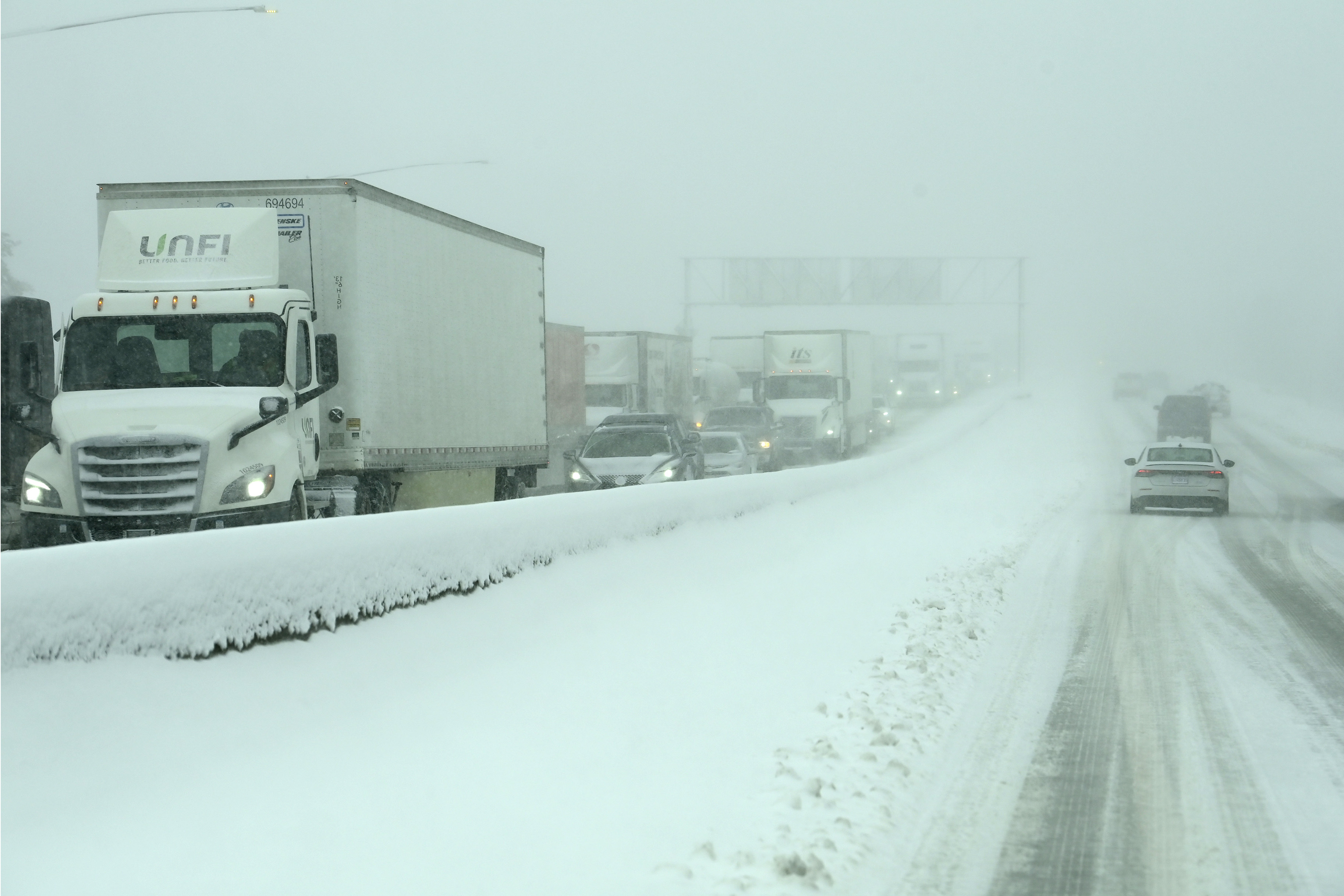 Semi-trucks and cars sit parked on a snowy freeway