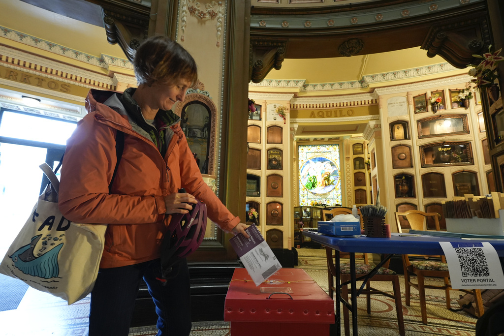 A woman is casting her ballot in a lavishly decorated room, filled with wooden cabinets and a stained glass window.