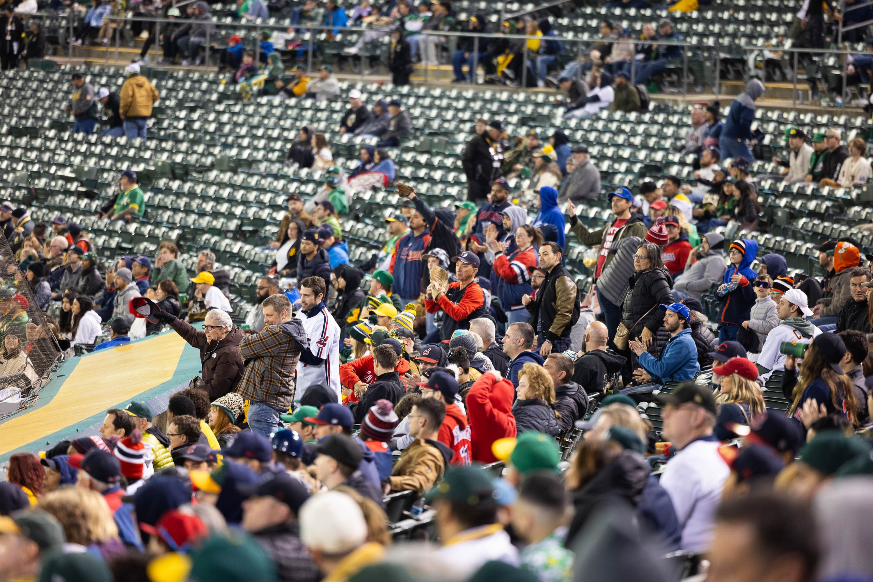 The image shows a stadium filled with enthusiastic, bundled-up spectators, many of whom are standing and cheering, possibly at a baseball game.