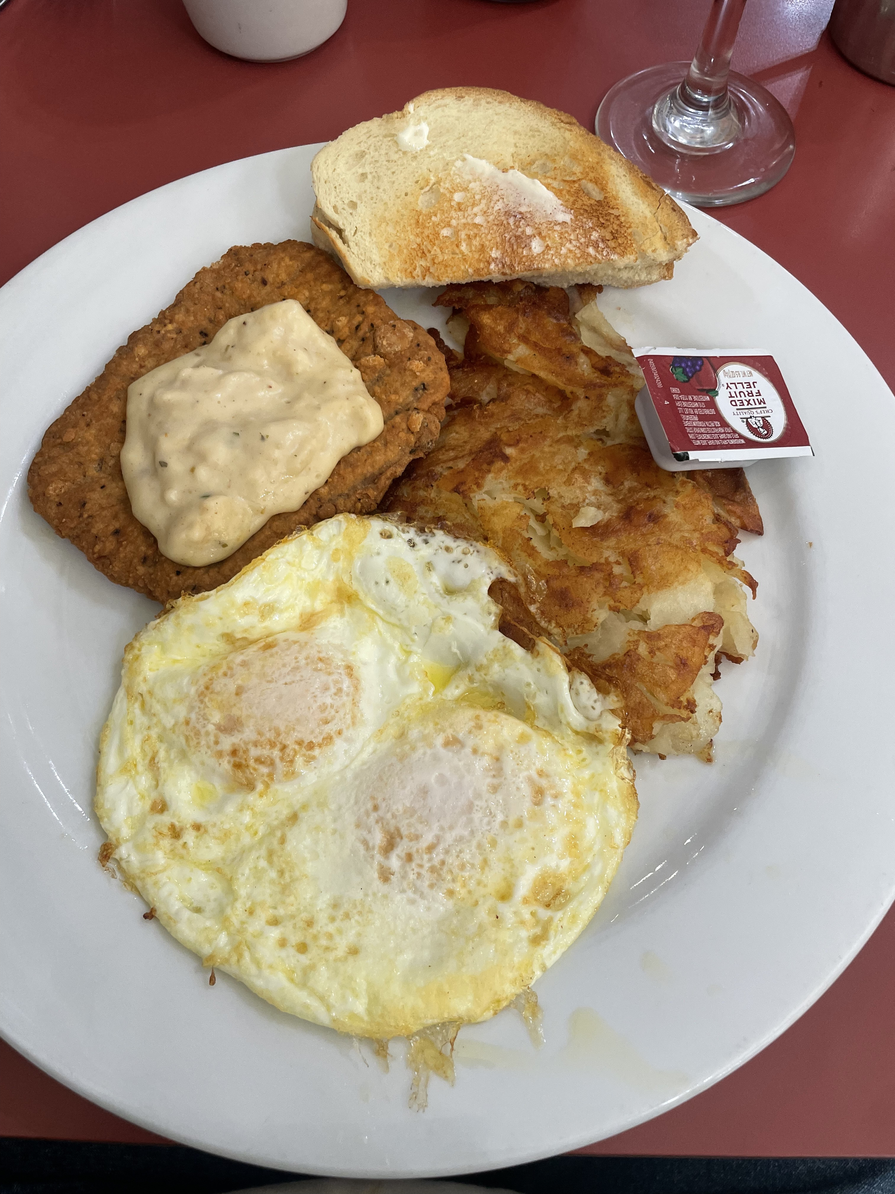A plate with eggs, hash browns, fried chicken, gravy, toast, and a jelly packet.