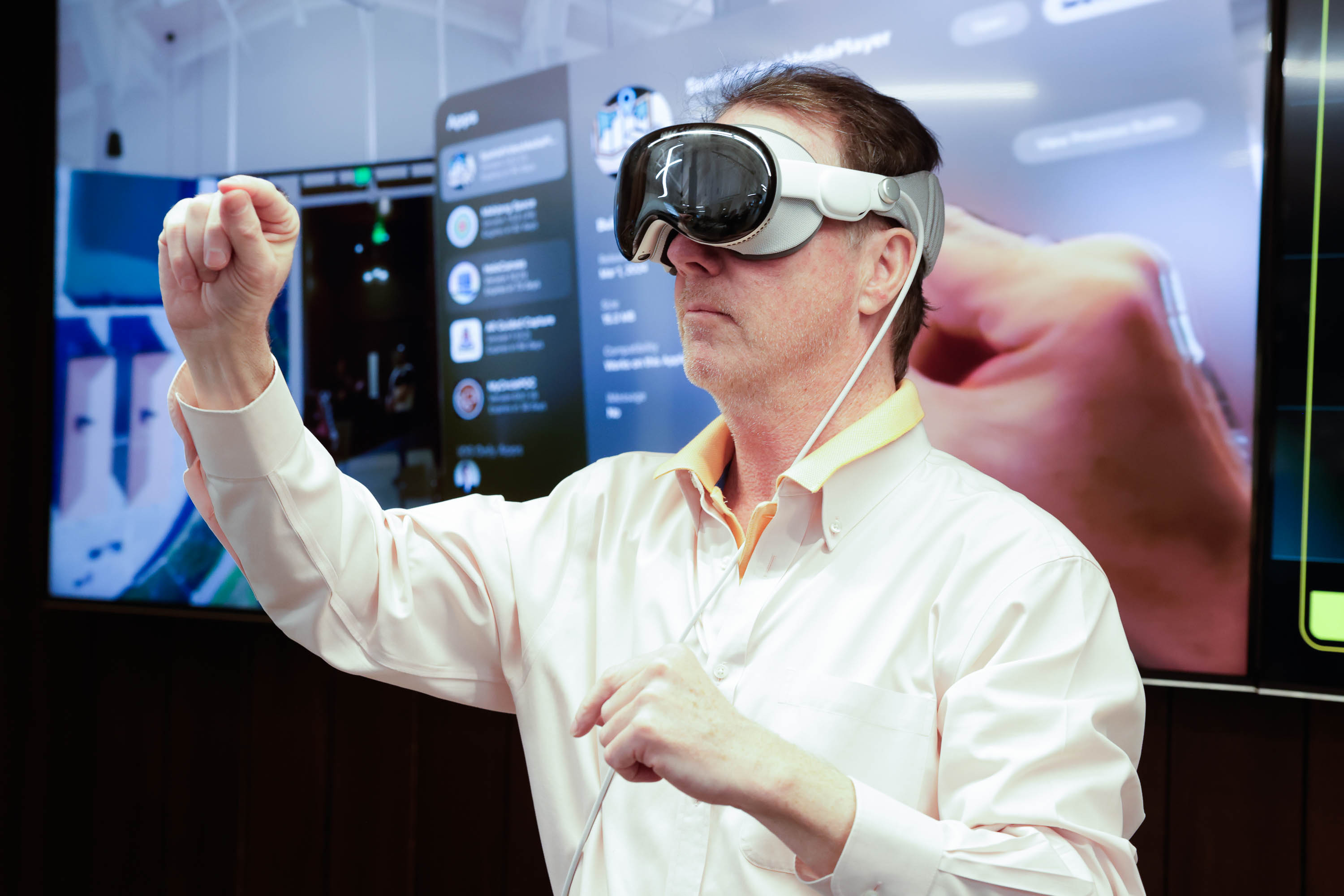 A man in a Apple Vision Pro headset gestures his hands into the air as screens display tech interfaces in the background.