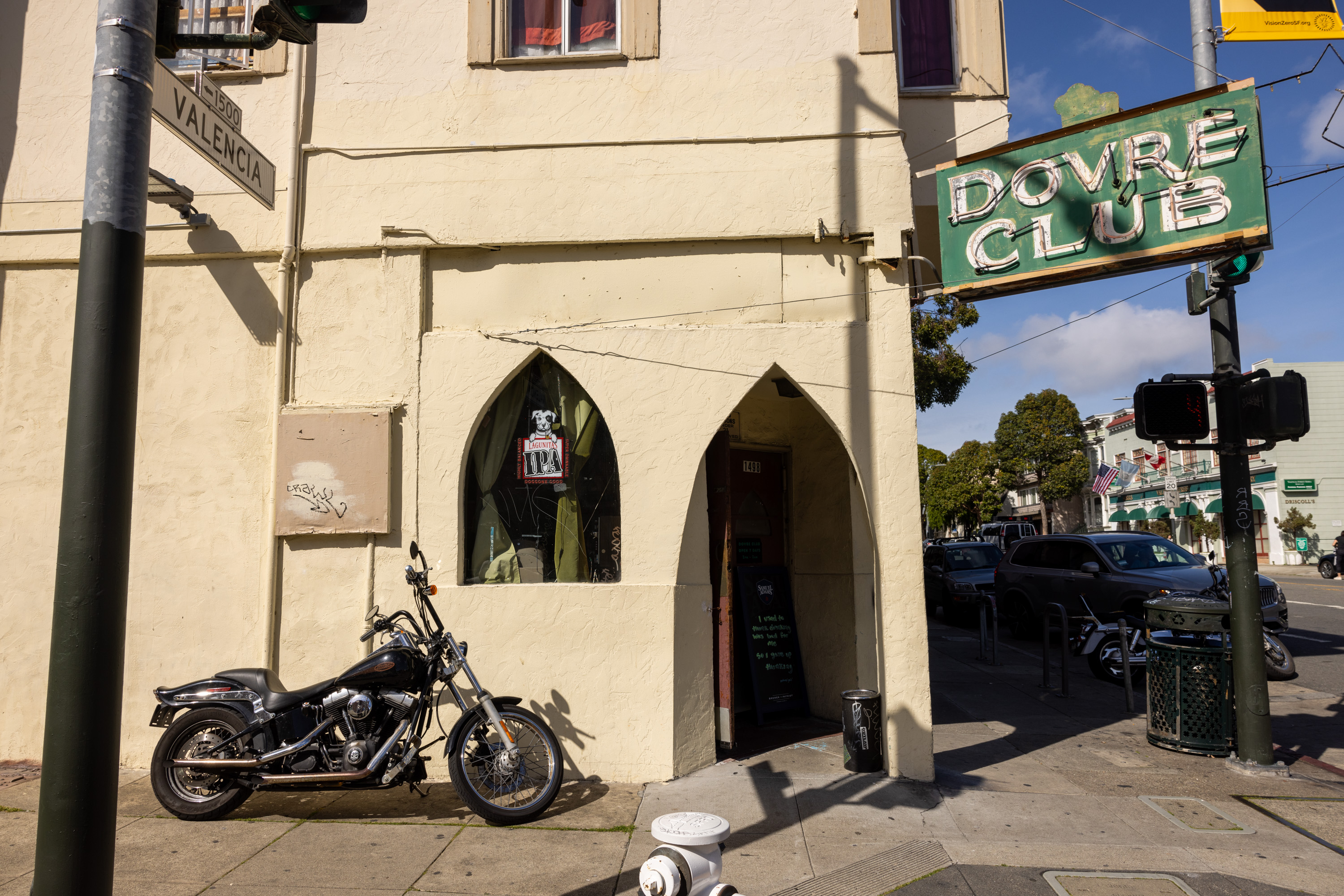 A motorcycle is parked by a corner building with a "Dovre Club" neon sign, near a street sign for Valencia.