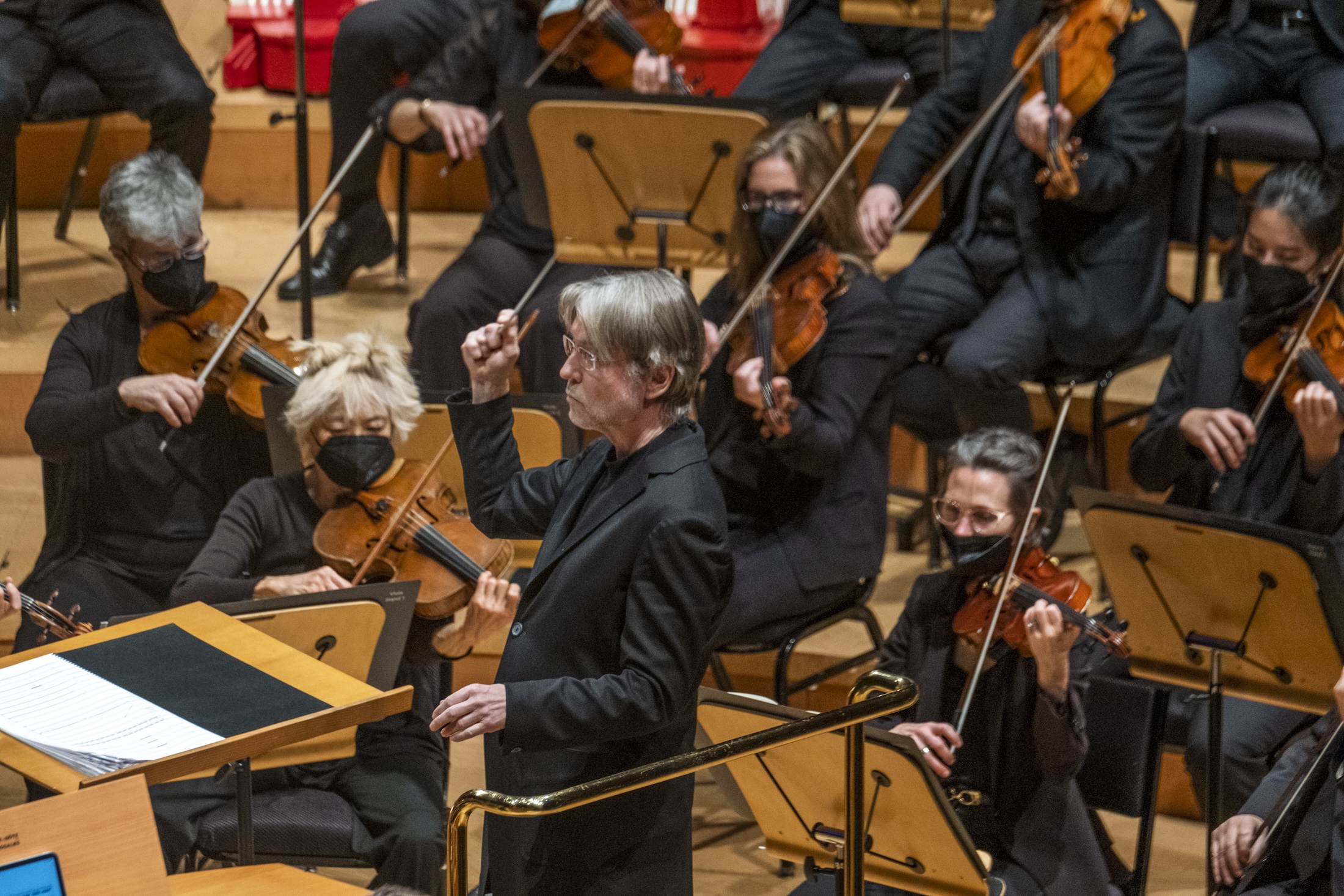 A conductor leads an orchestra of masked violinists, evoking a performance in a pandemic era.
