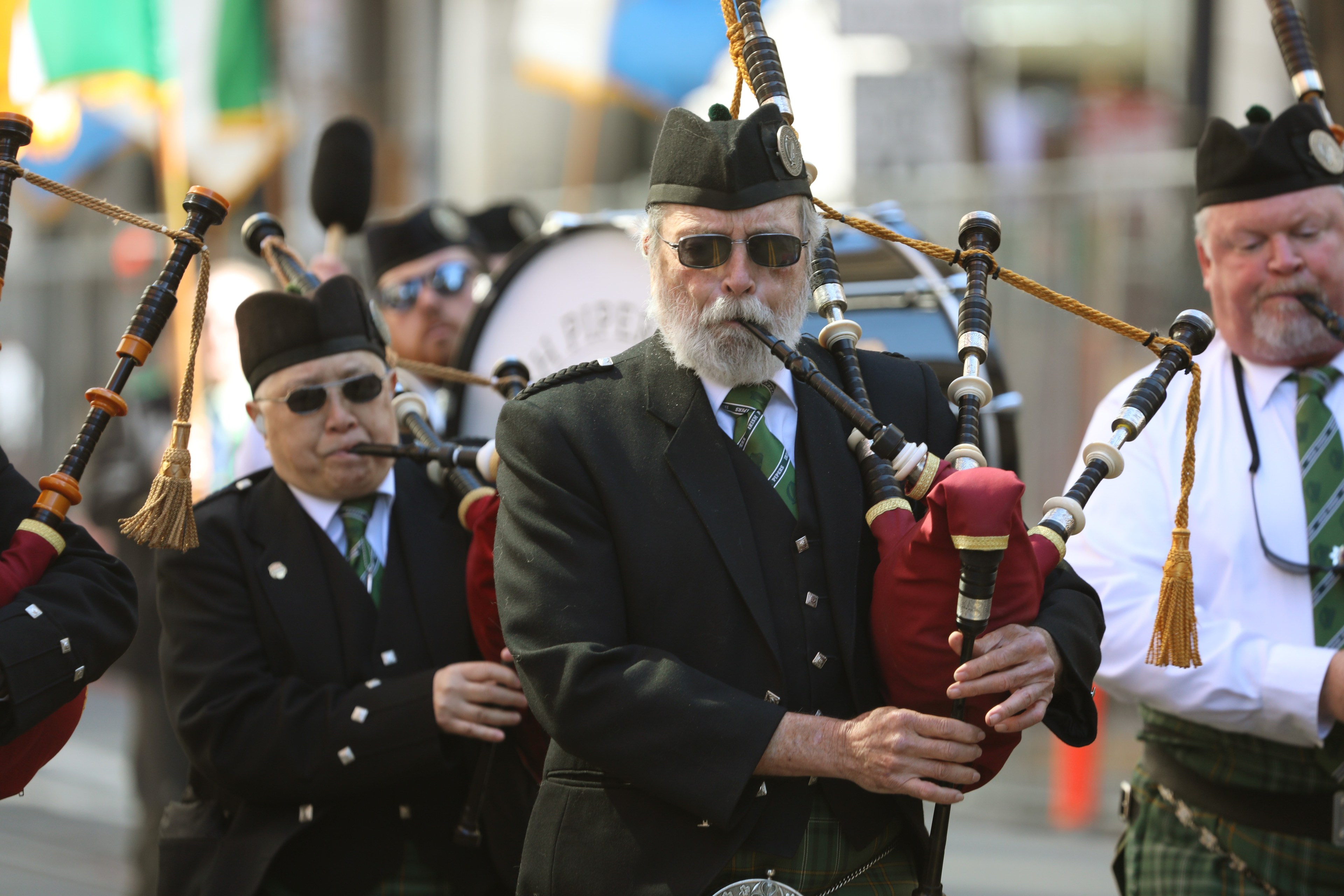 Men in traditional Scottish attire play bagpipes in a parade.