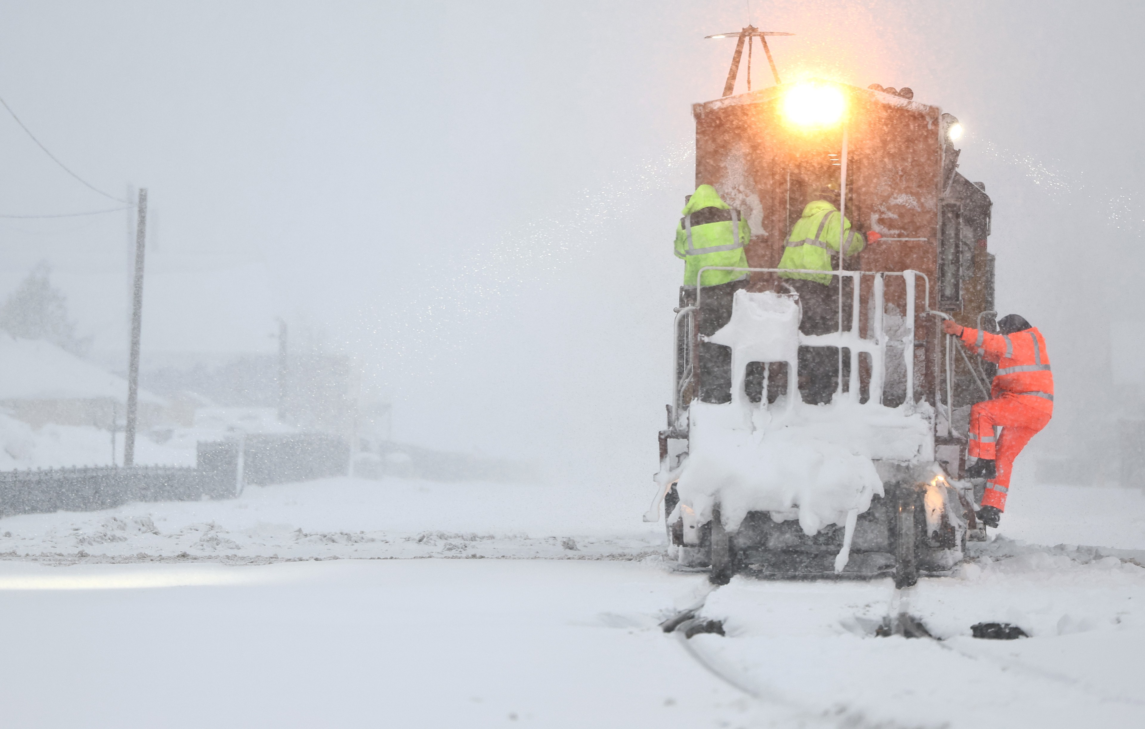 Train workers climb onto back of train moving through snowy scene