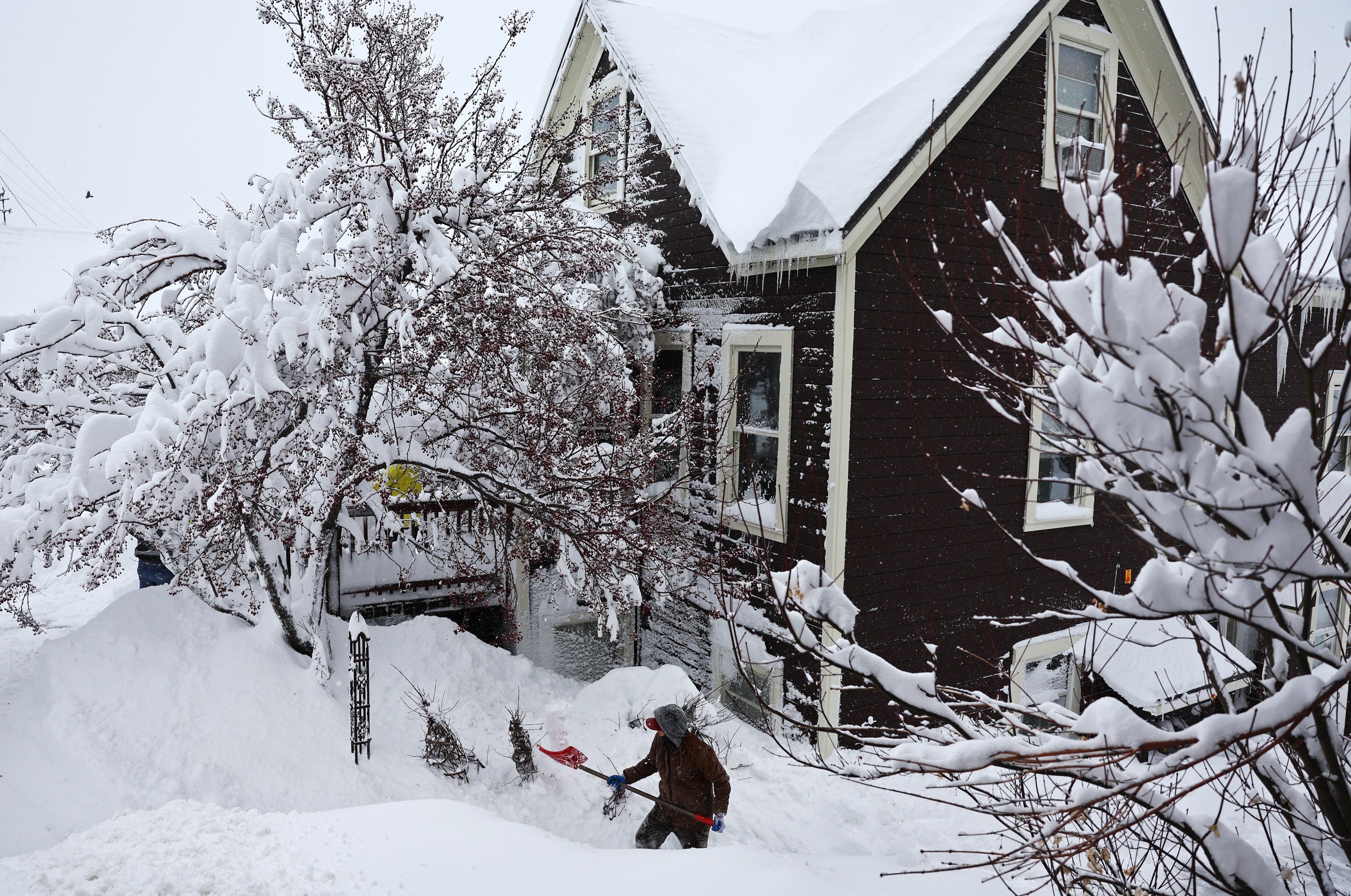 A worker digs through a pile of snow outside a snow covered building