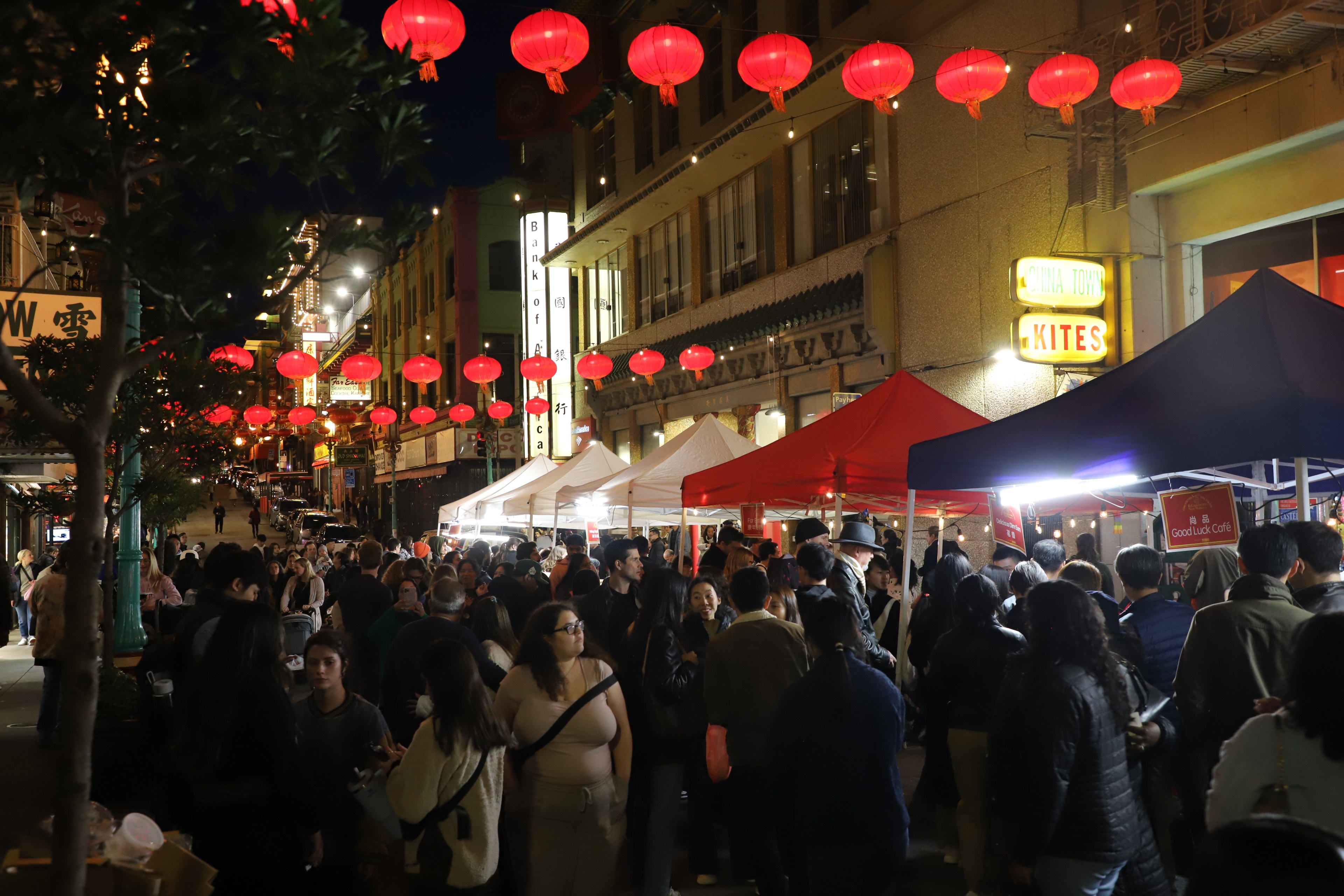 A bustling night market with red lanterns, crowds, and street vendor tents.