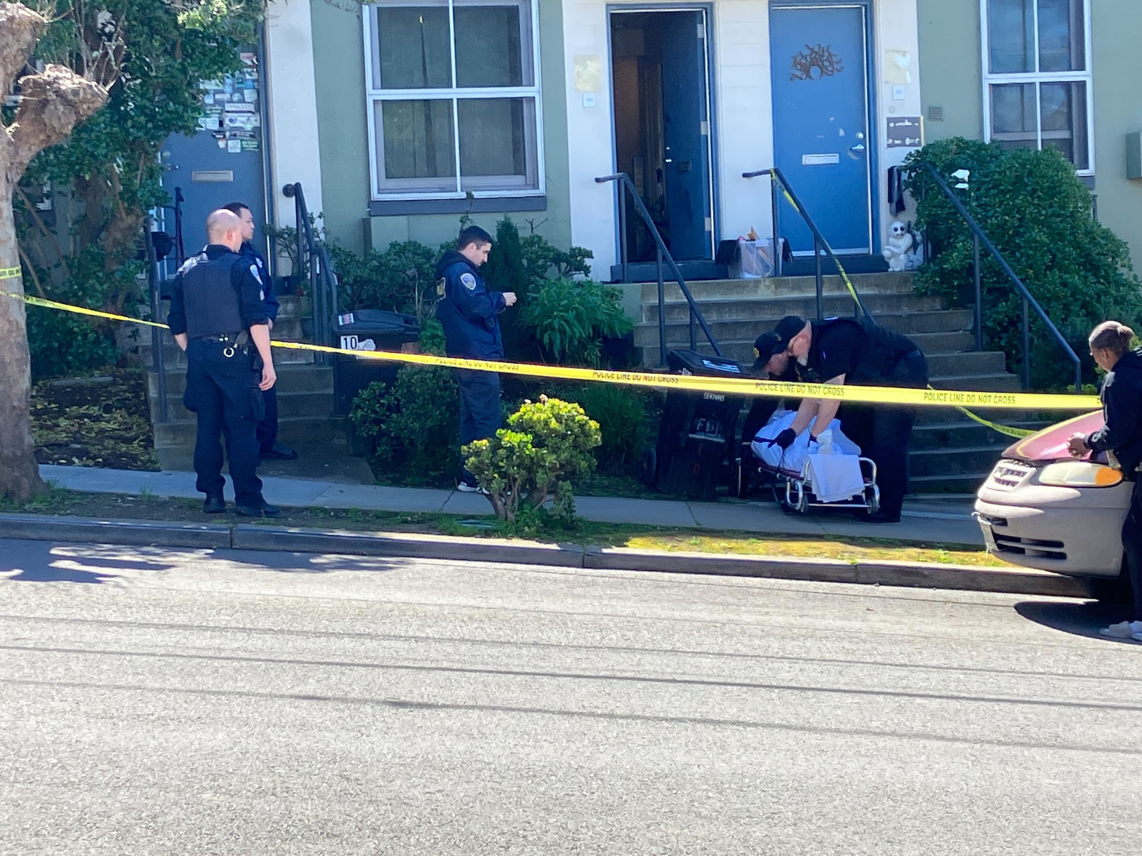Police officers and taped-off scene with a dog watching from a doorway.