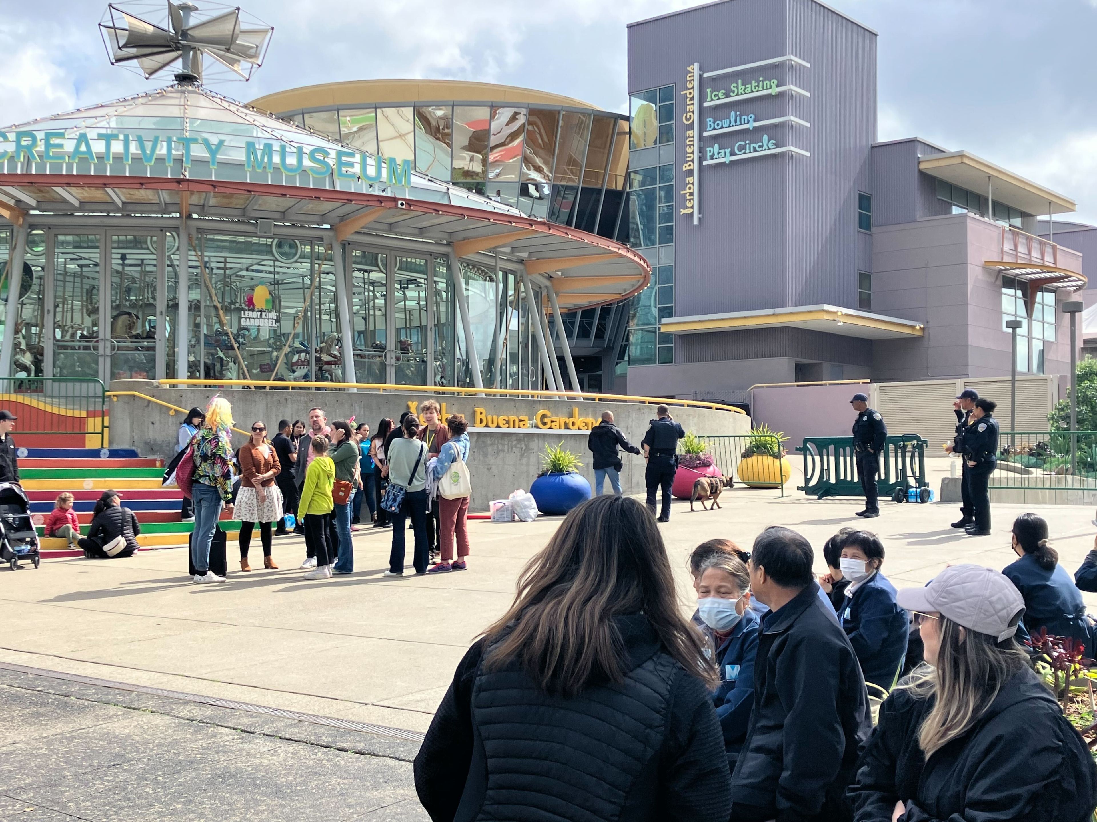 A crowd gathers outside the "Creativity Museum," with police officers nearby, under a partly cloudy sky.