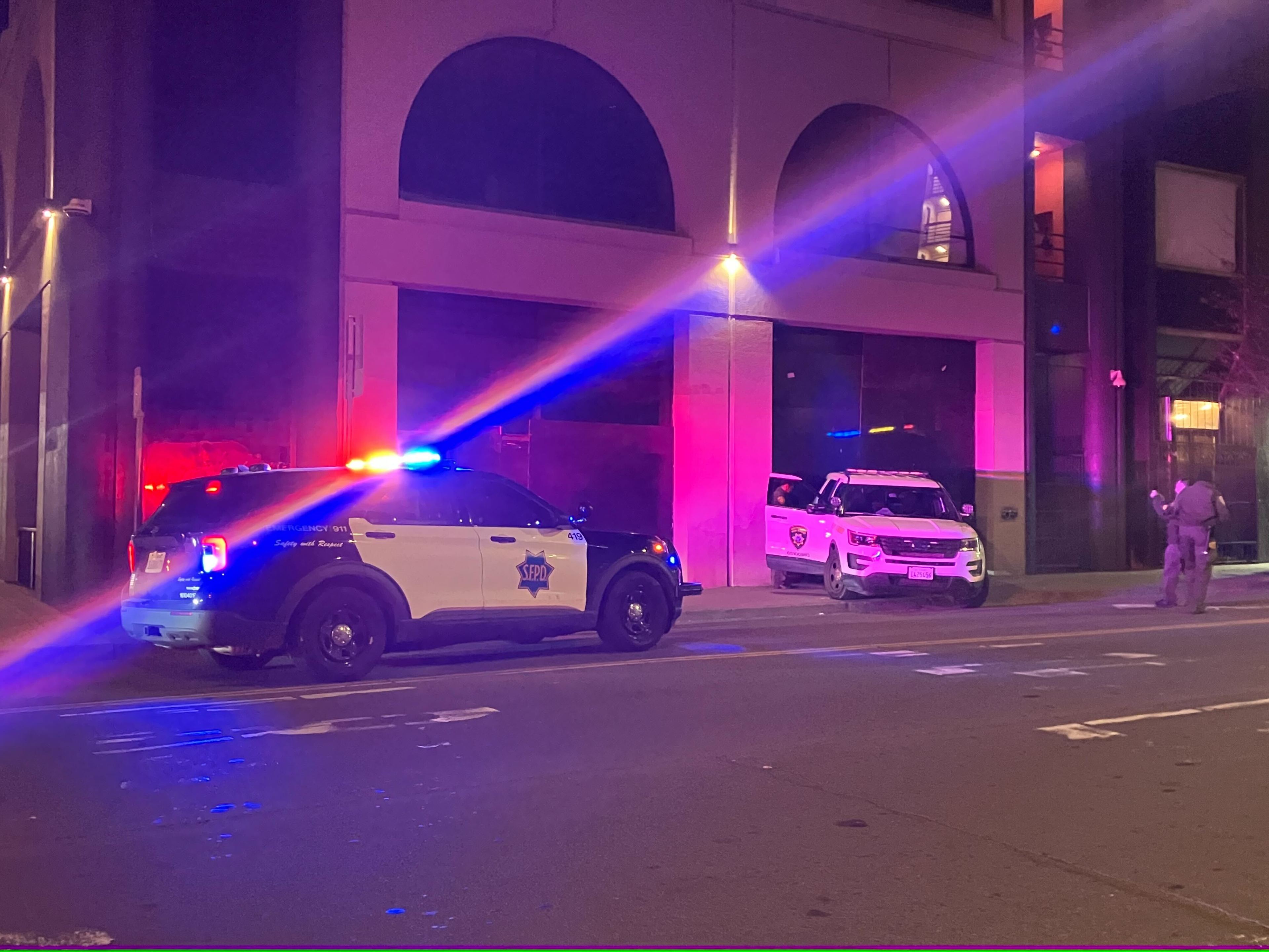 An SUV backed into a building rests on a sidewalk, with police officers investigating.