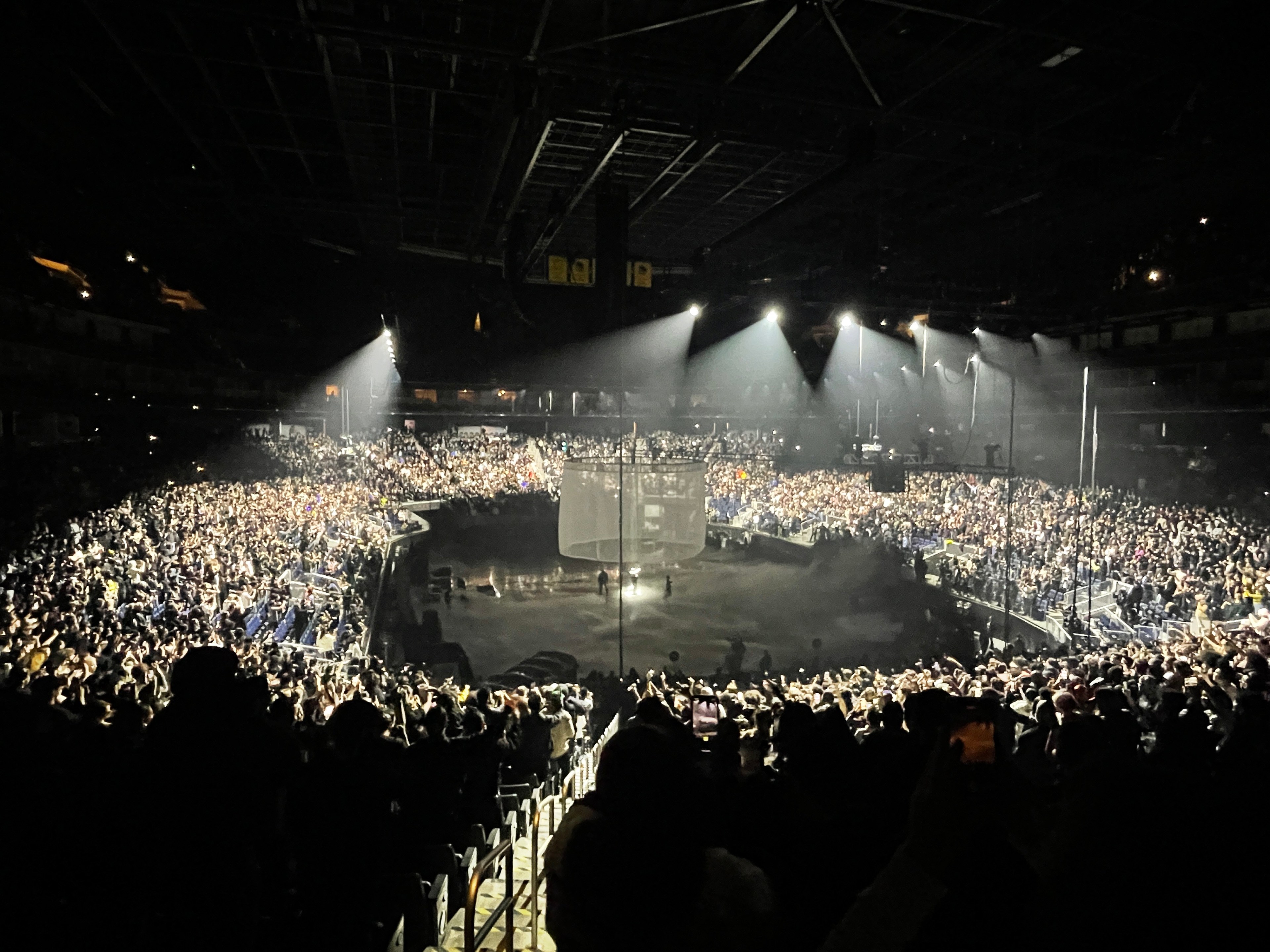 A concert arena filled with a large crowd, lit by stage lights, before or after a performance.