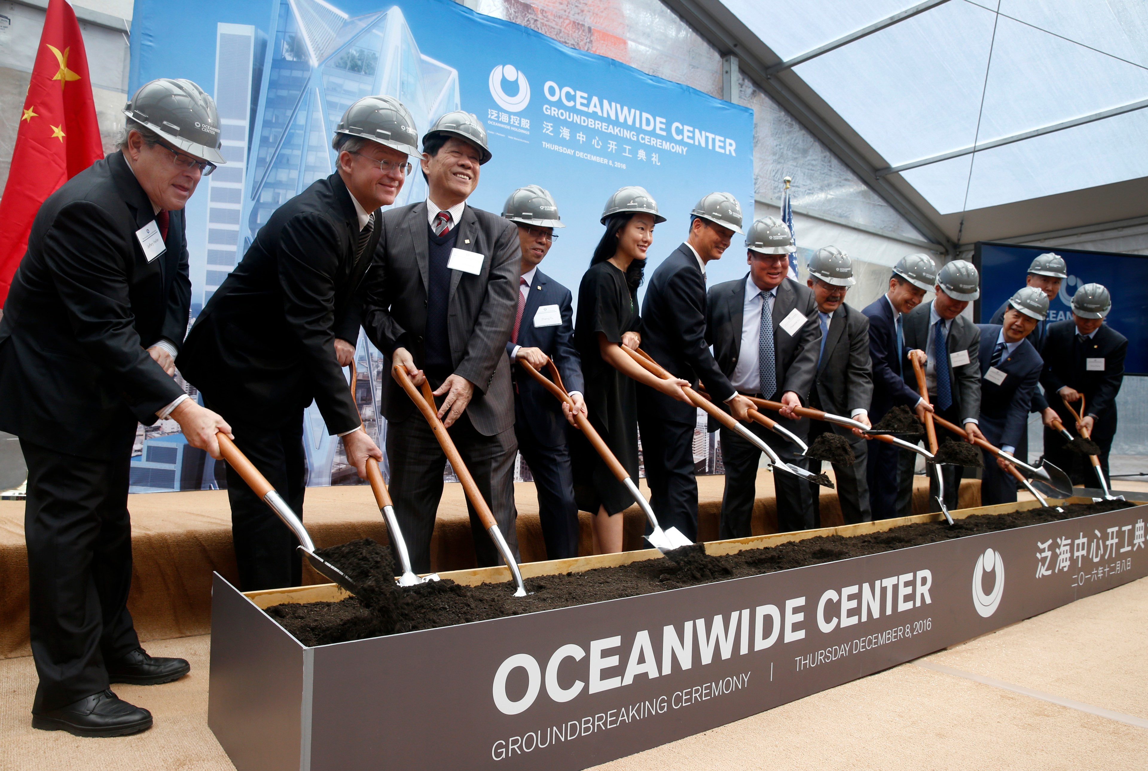 Group of people in suits and hard hats at a ceremonial groundbreaking.