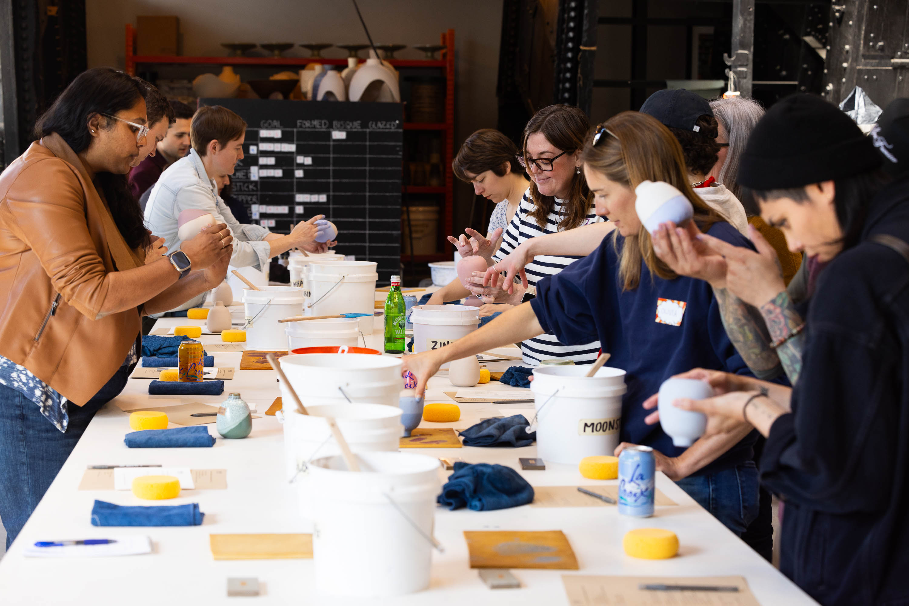 A group of people is engaged in a pottery painting workshop, focusing on their individual pieces.