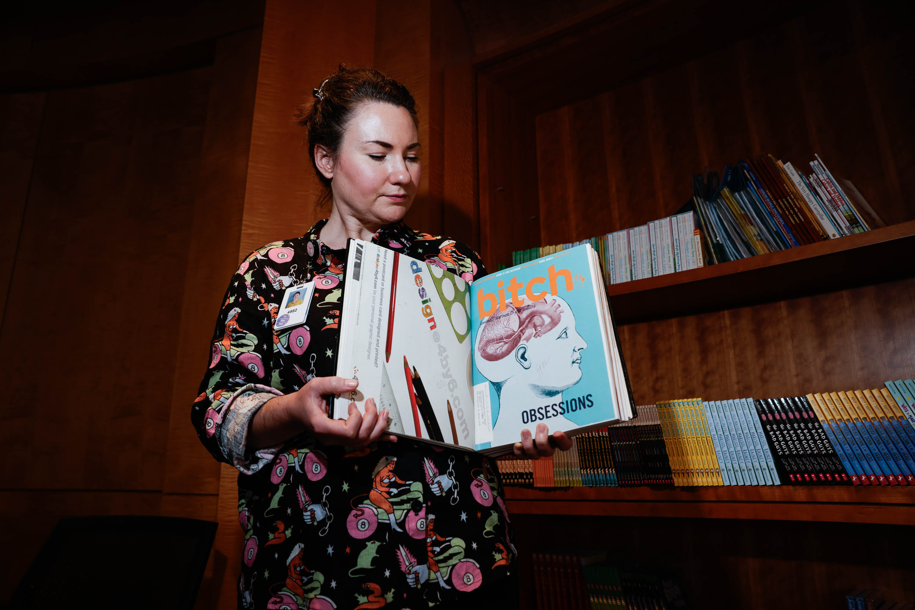 A woman holds up a Bitch magazine with a shelf of colorful books behind her.