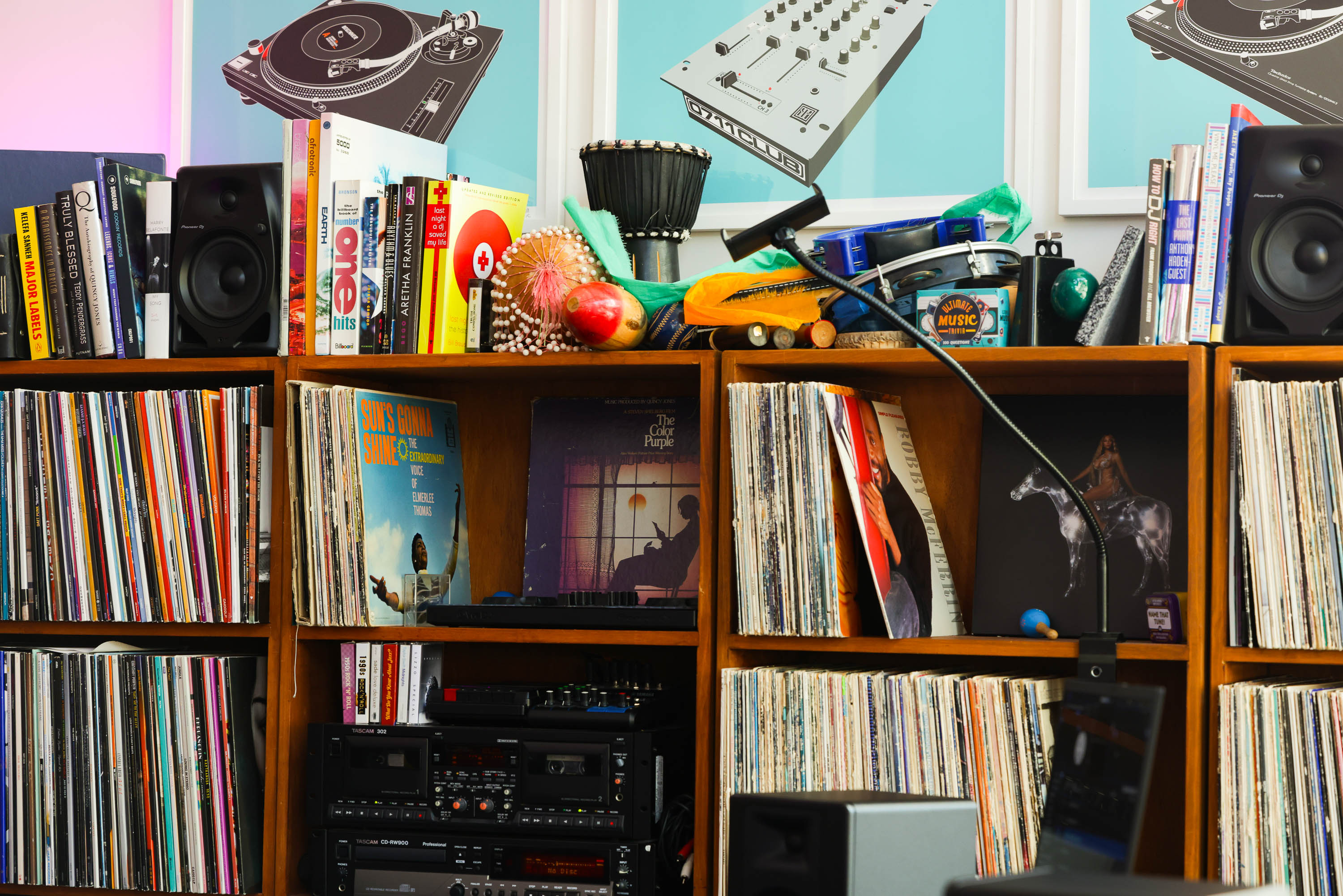 A wooden shelf filled with vinyl records, stereo equipment, books, and musical instruments against a blue wall.