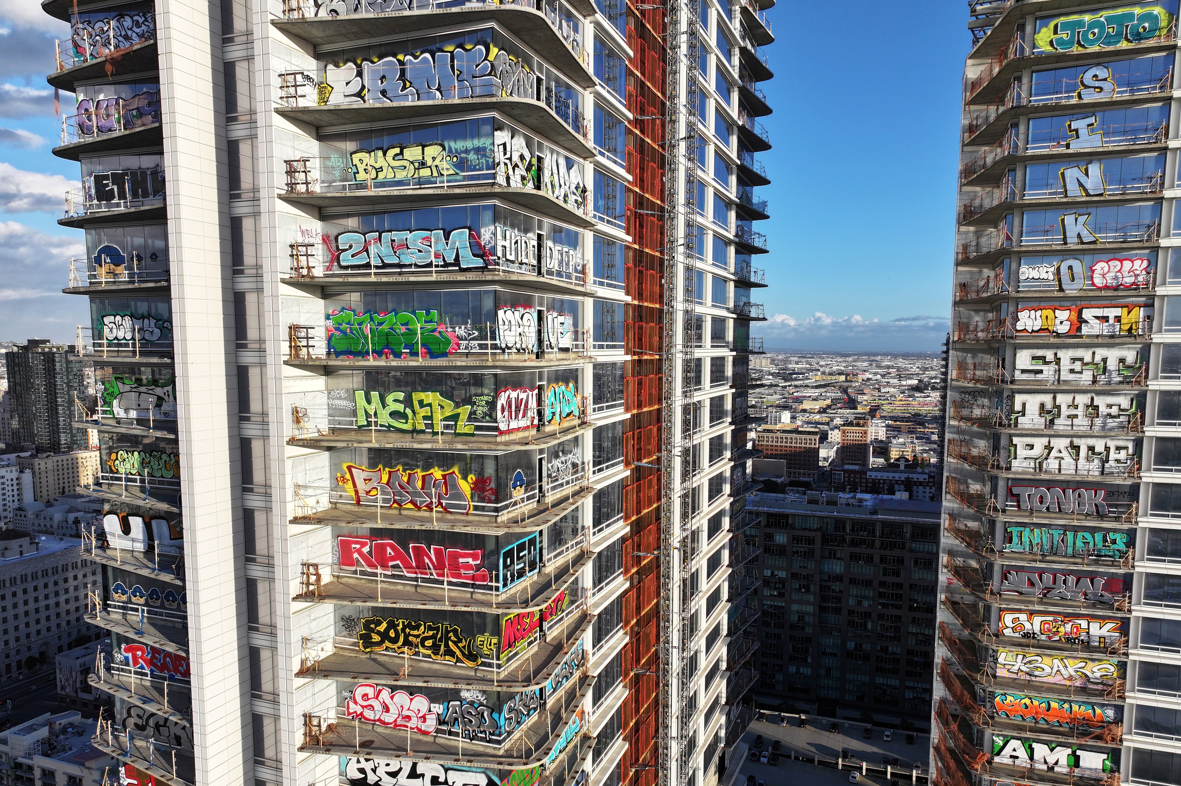 Two high-rise buildings covered in colorful graffiti with a cityscape and clear sky in the background.