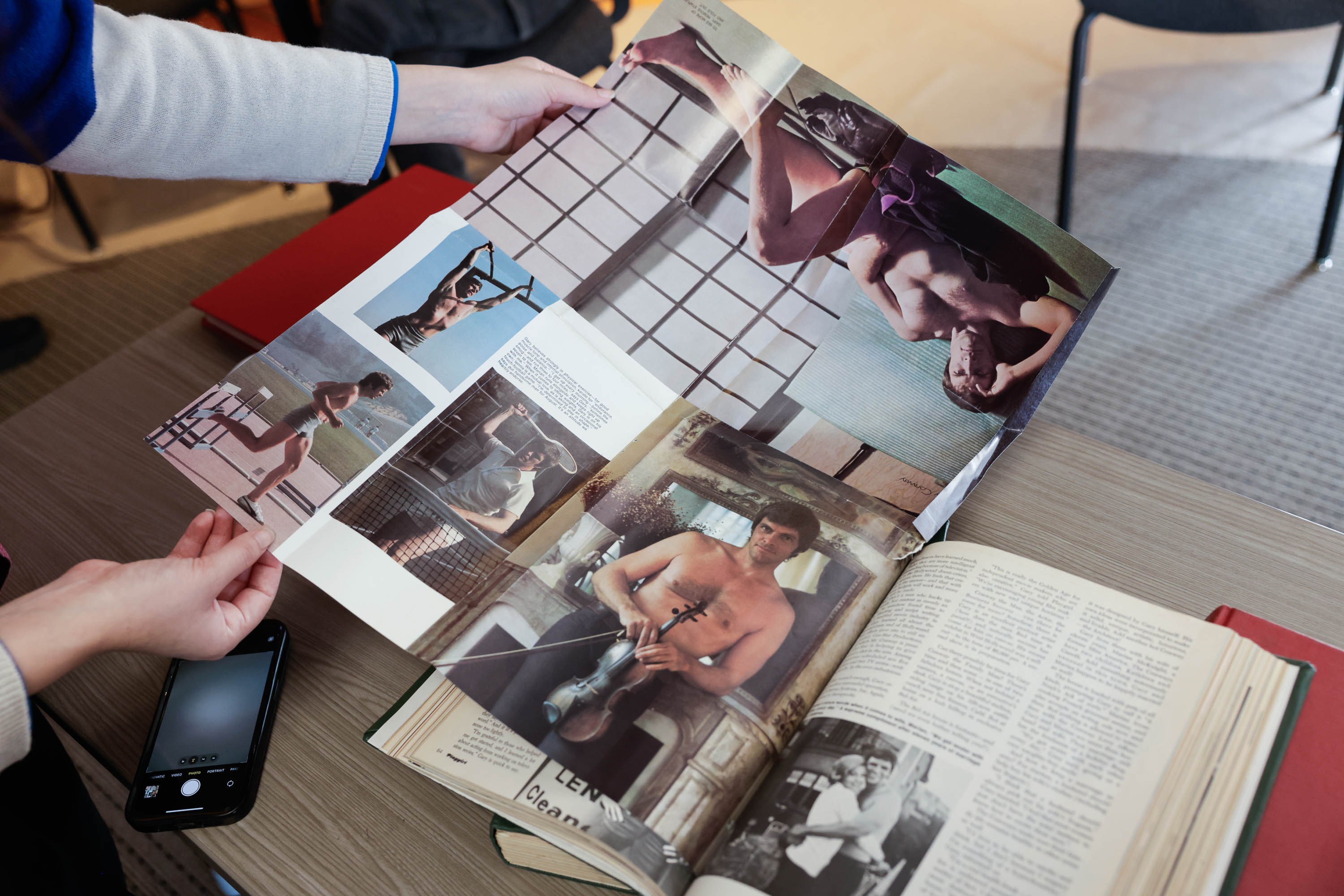 A person holds a magazine with various images of a shirtless man, including him playing a violin.