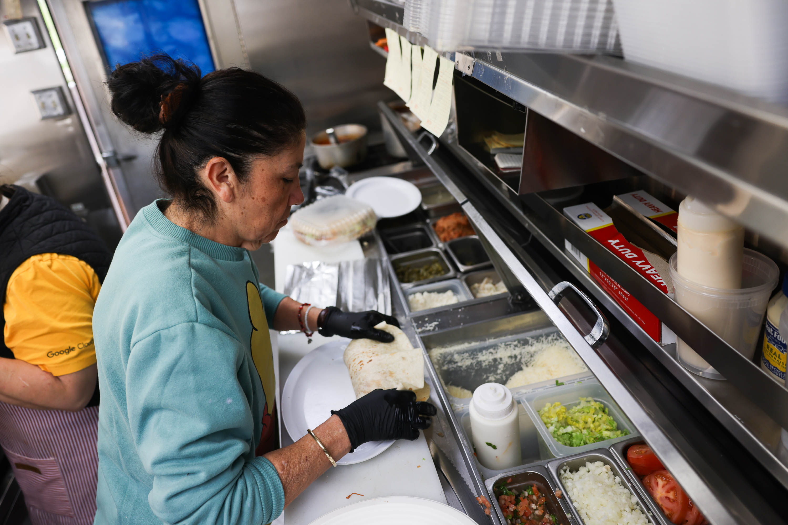 A person is making a burrito in a kitchen with various ingredients on display.