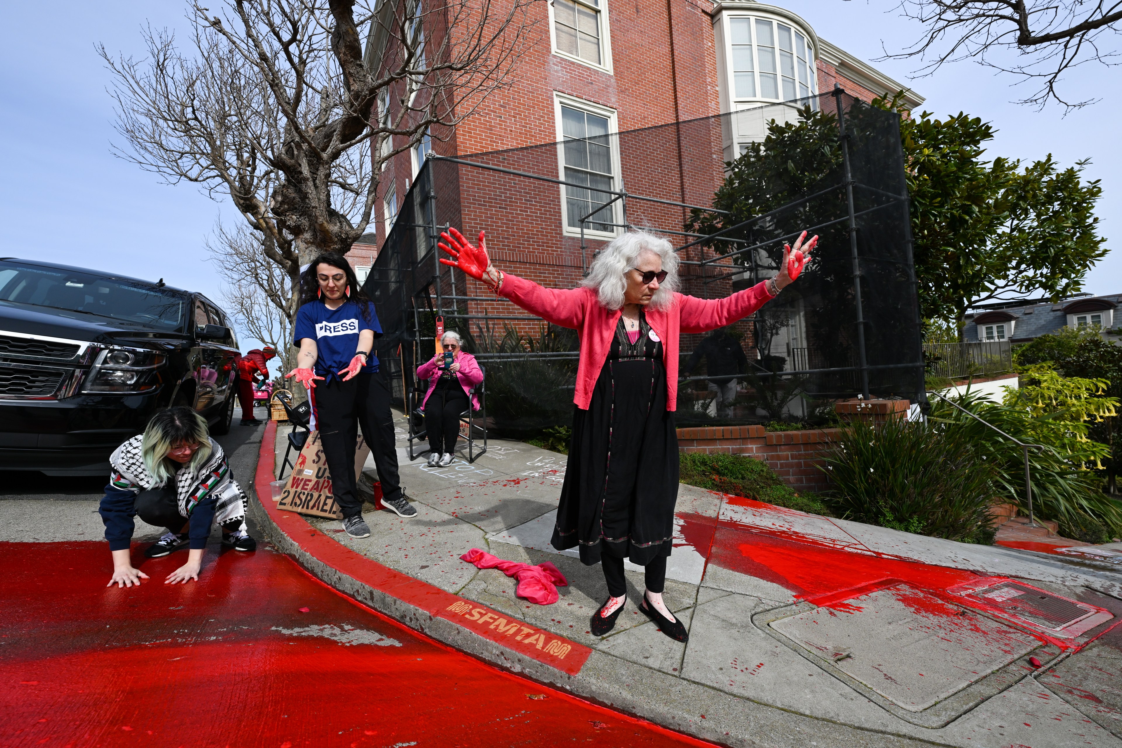 A woman with her hands raised in the air and red paint on the surrounding sidewalk