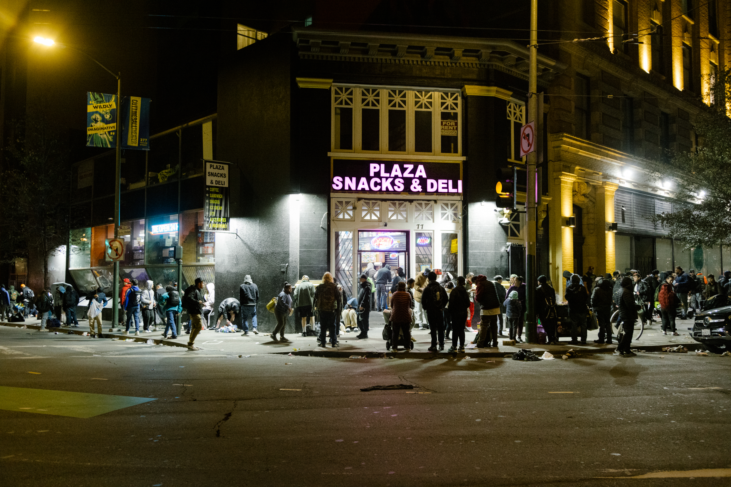 A bustling night scene outside 'Plaza Snacks & Deli', with a crowd of people on the sidewalk.