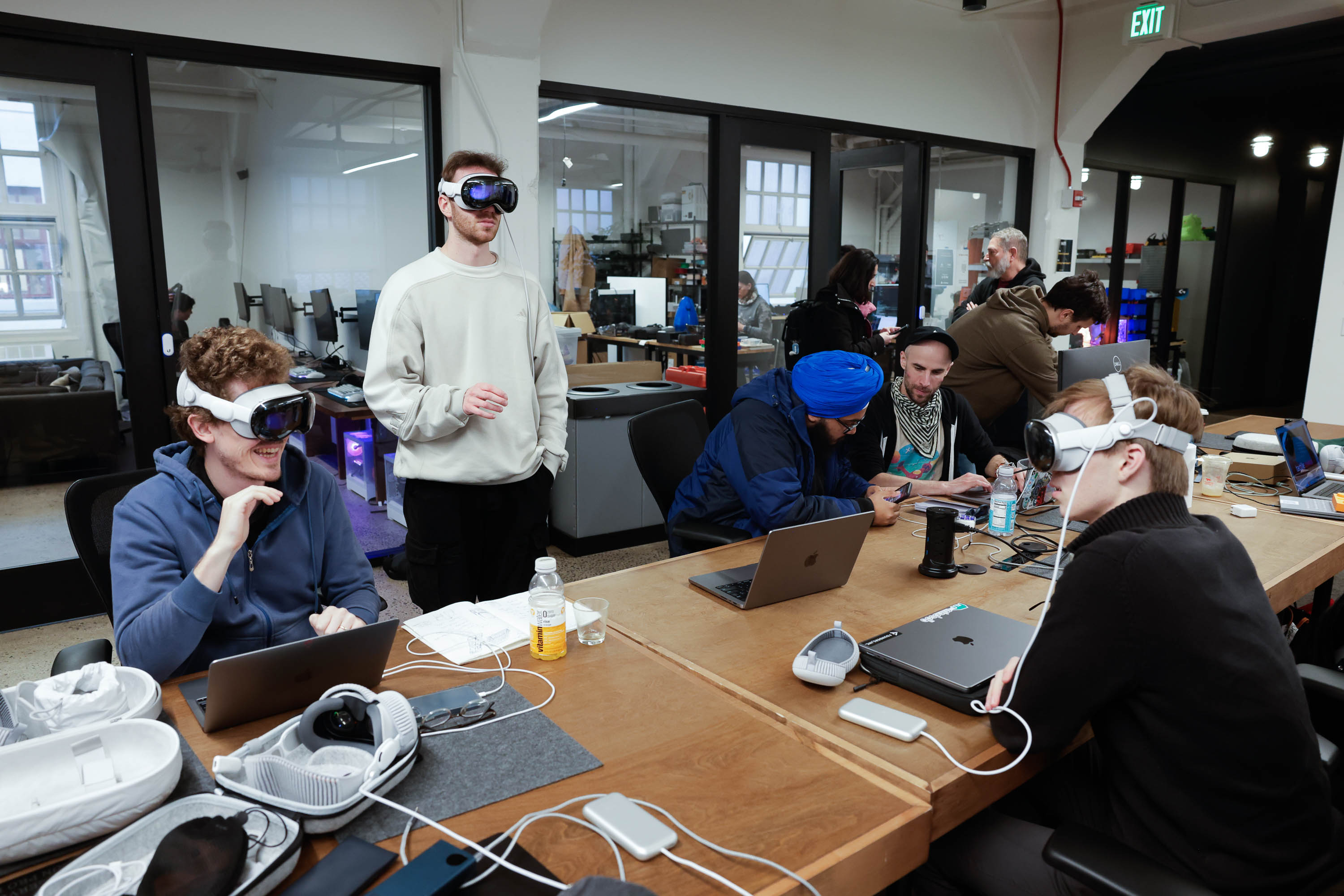 People work in a collaborative tech workspace and use Apple Vision Pro headsets and computers.