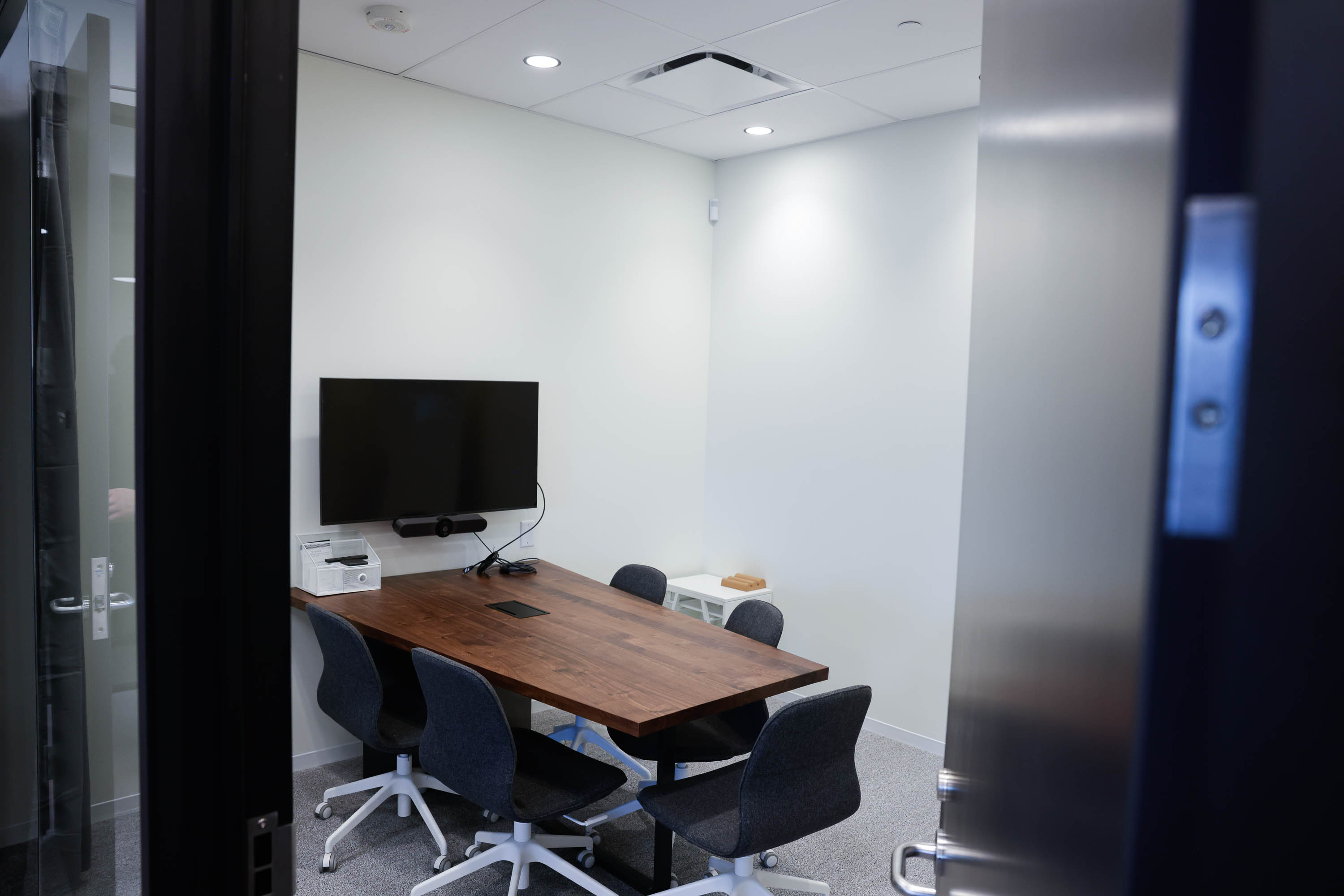 A modern conference room with a wooden table, chairs, and a monitor on the wall.