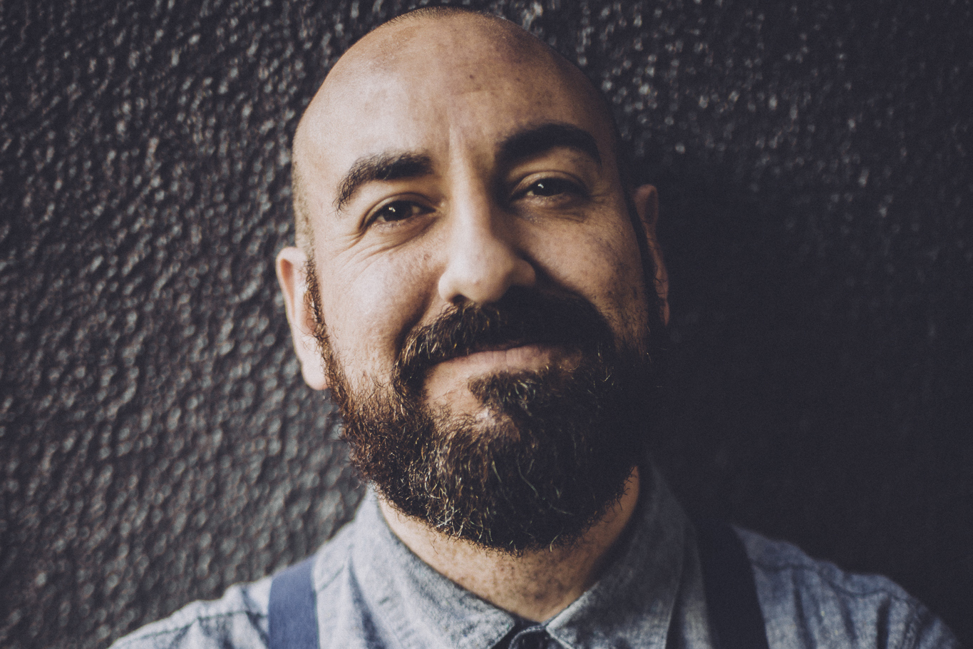 a bald, bearded white man in a blue collared shirt smiling