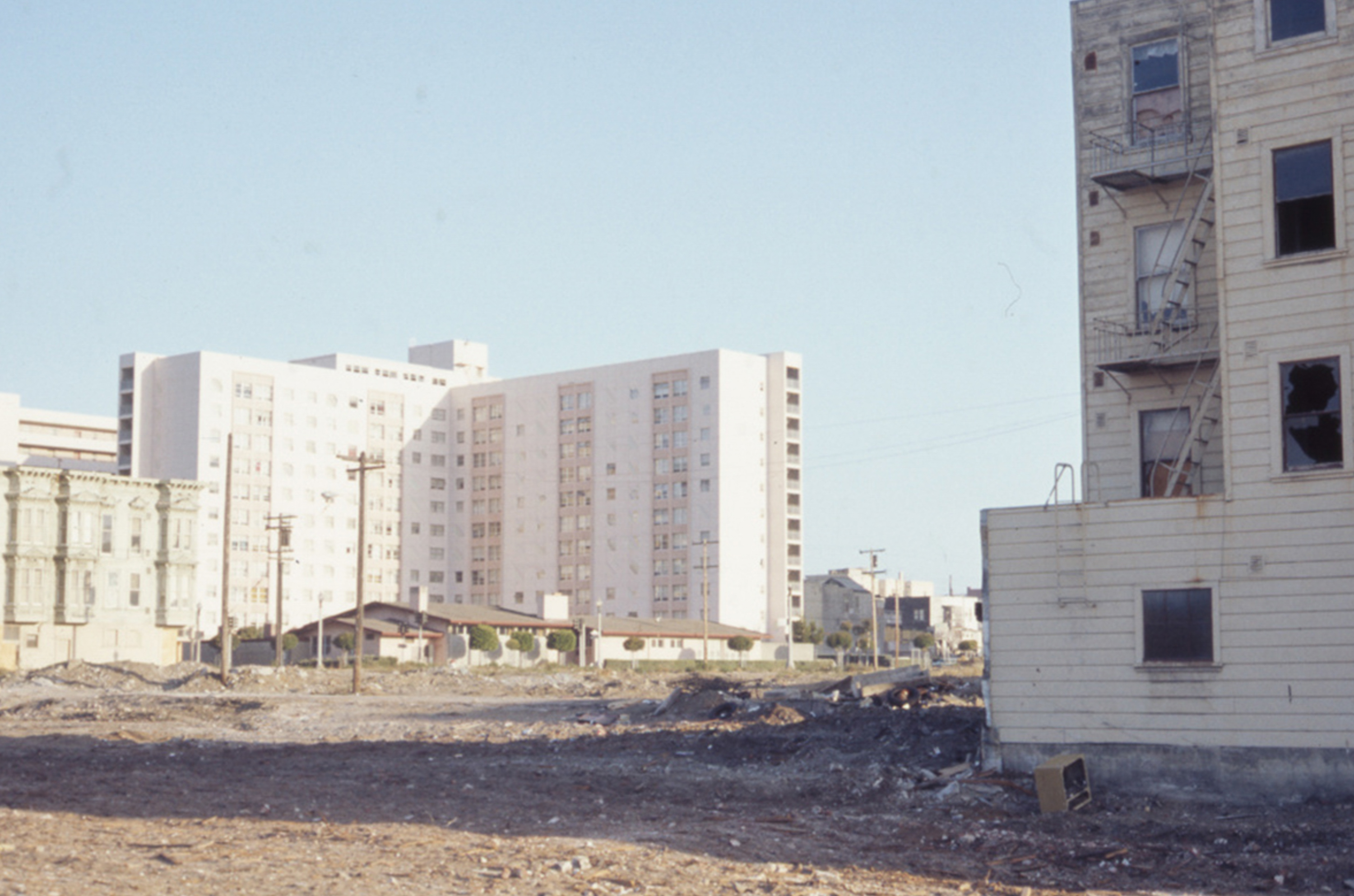 Apartment buildings behind a barren lot with debris, suggesting recent demolition or construction.