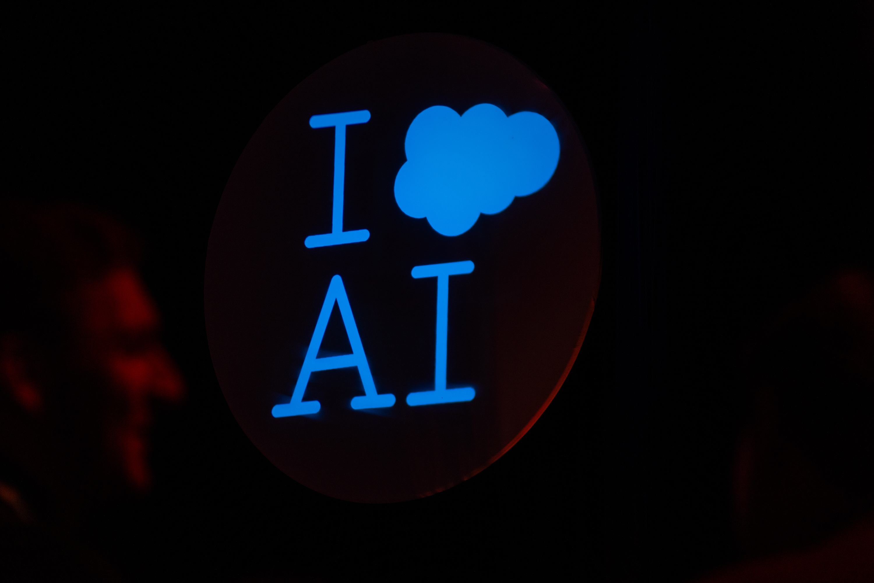 A glowing sign reads &quot;I ♥ AI&quot; against a dark background, with a heart symbol replaced by a cloud icon.