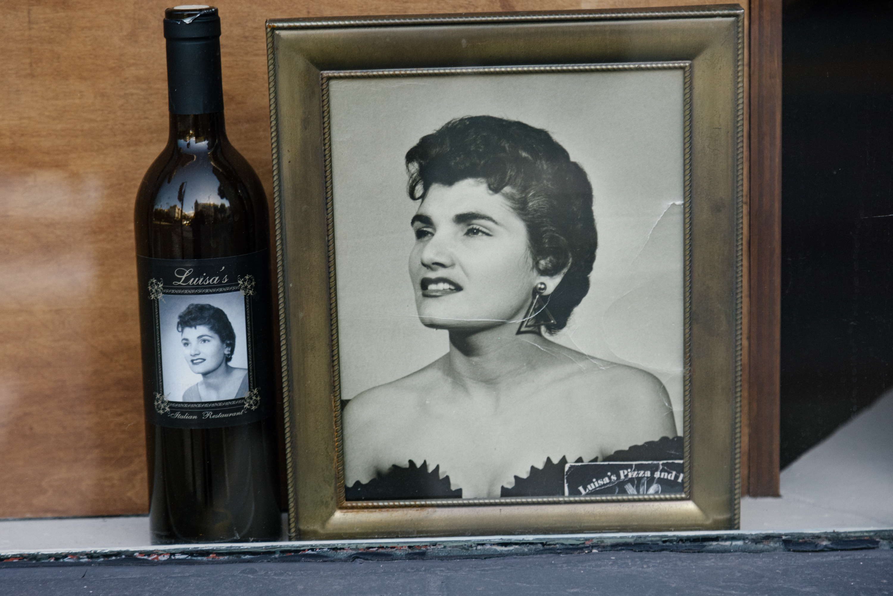 A framed black-and-white portrait of a smiling woman next to a wine bottle with a similar image label.