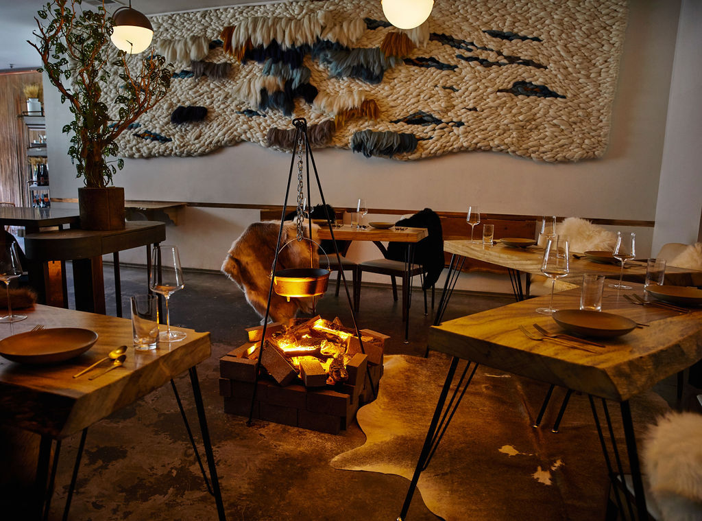 a dimly lit, intimate restaurant interior with a large woven art piece on the far wall