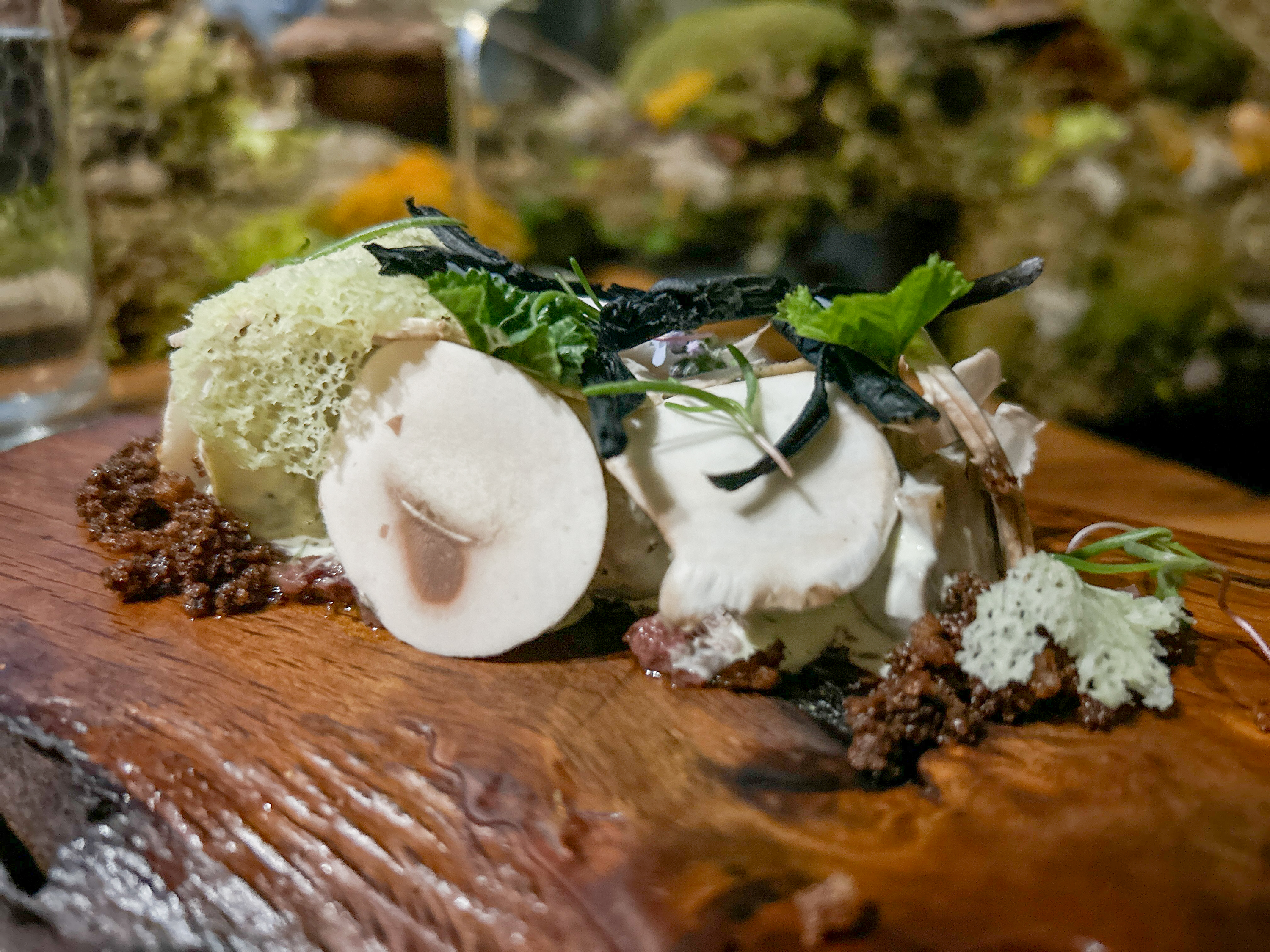 Gourmet dish with mushrooms, foam, herbs on a wooden board.
