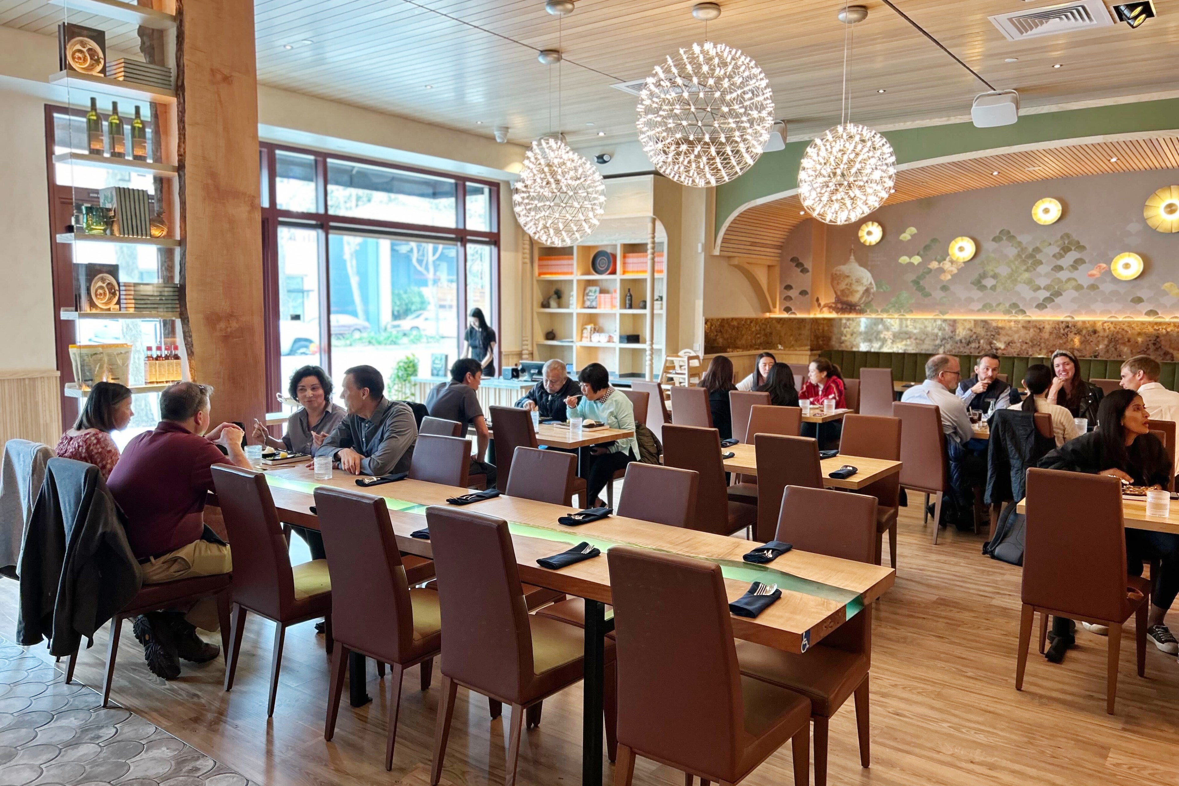 A busy restaurant interior with diners at tables and modern decor, including spherical chandeliers.