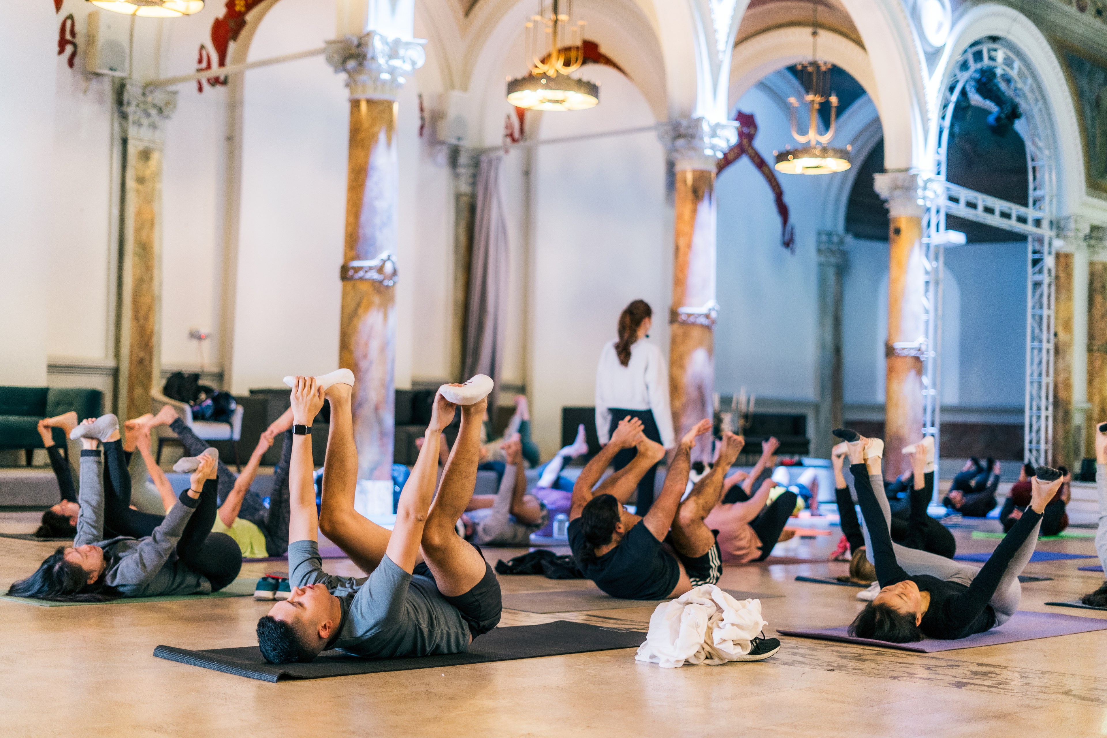 A group is practicing yoga in an elegant, high-ceilinged room with arched windows.